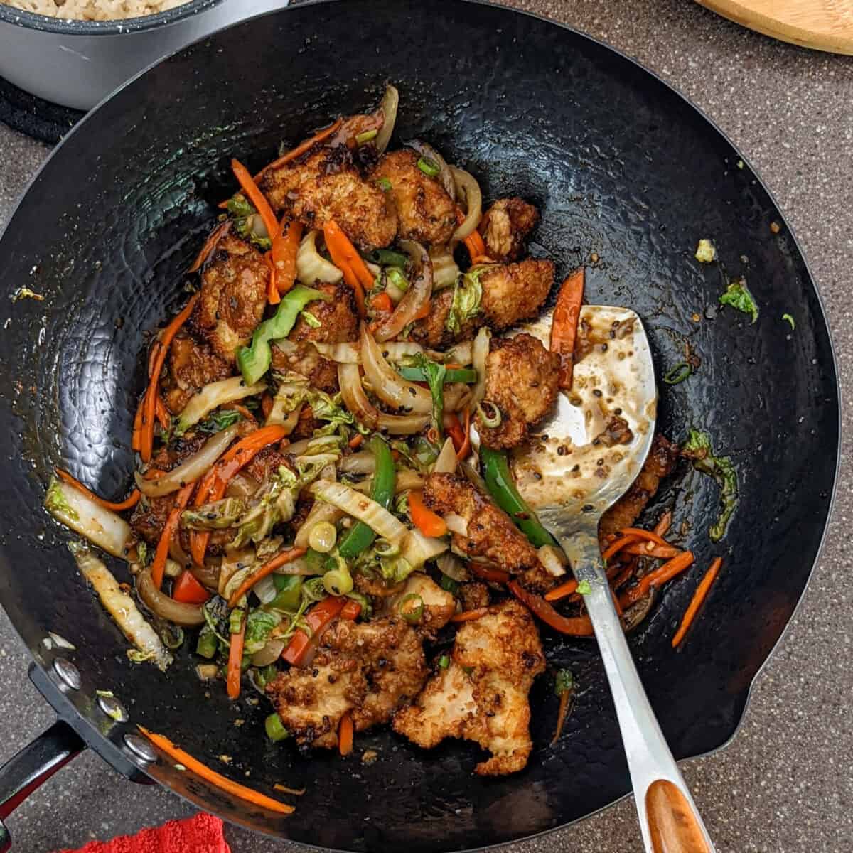 hot honey sesame chicken with juilienne vegetables in a wok