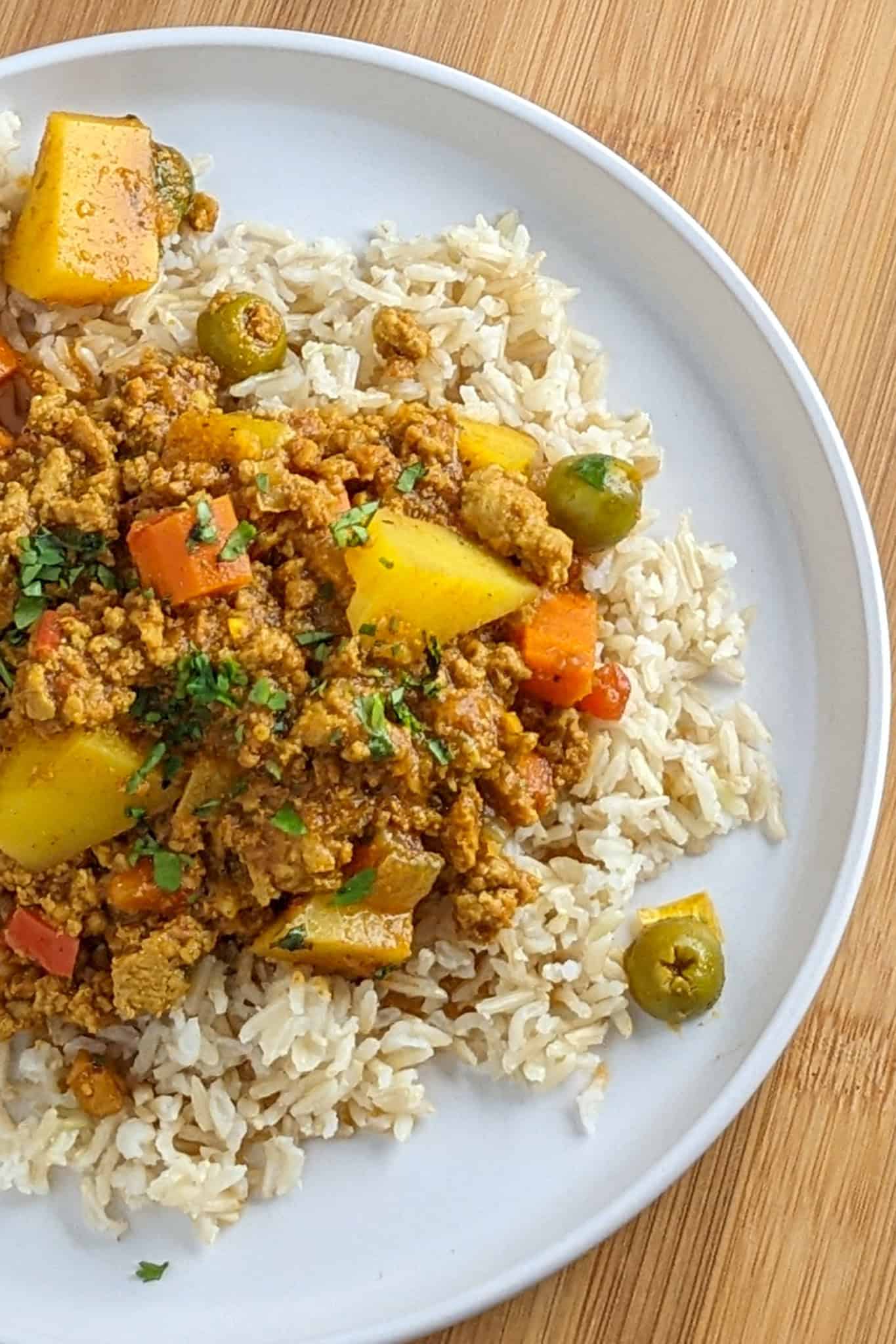 top view of the plated ground turkey picadillo made up of Jamaican curry seasoned ground turkey cooked with potato chunks, olives, carrots, bell pepper and tomatoes on a bed of cooked brown basmati rice.