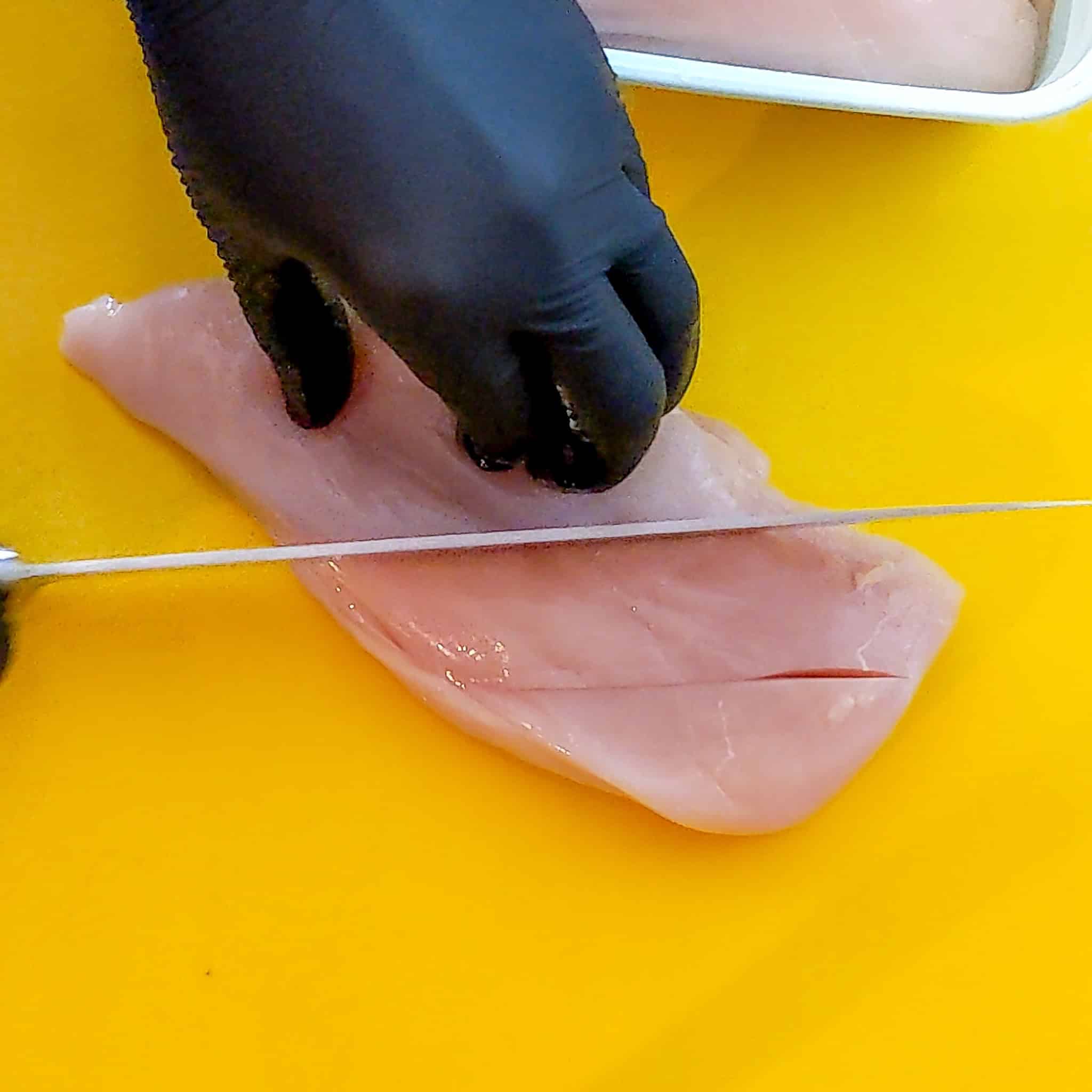 slitting chicken breast on a color coded cutting board with a knife.