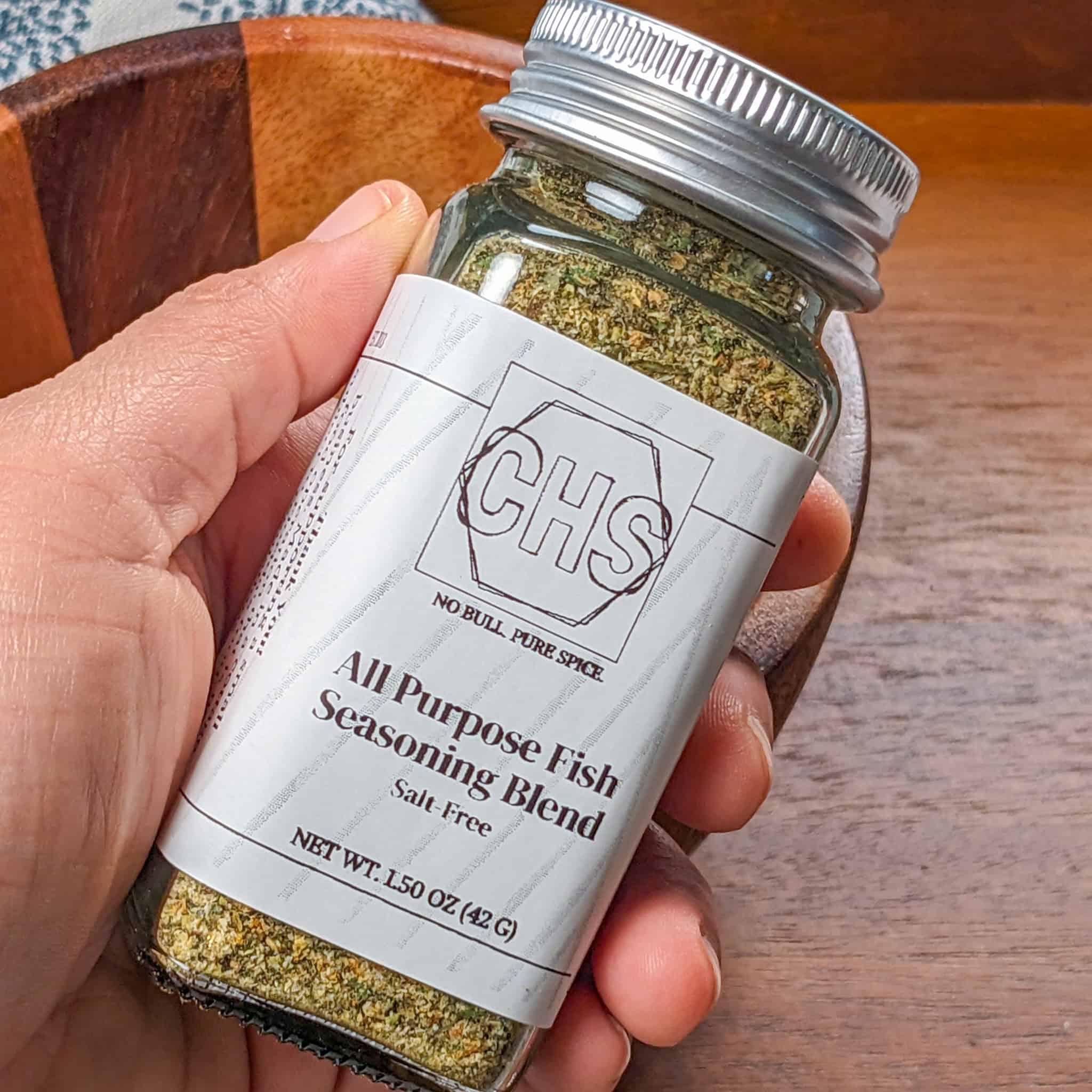 custom herb spice shop all purpose fish seasoning in a glass spice jar held in hand.
