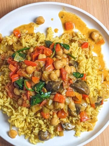 Vibrant chickpeas and vegetables curry over turmeric yellow rice on a white plate.