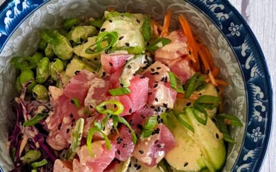 Raw Ahi Tuna surrounded by vegetables with a creamy sauce, decorated with sesame seeds and scallions