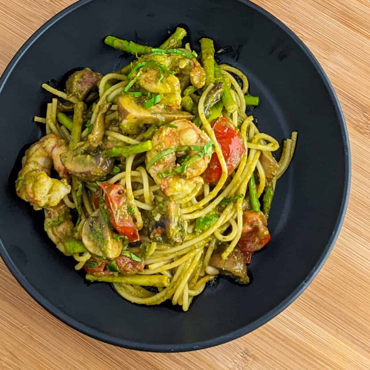 Pesto Shrimp Pasta with shrimp, tomatoes and asparagus in a black pasta bowl