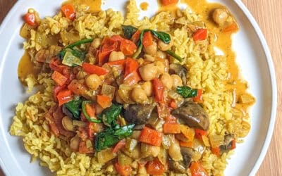 Vibrant chickpeas and vegetables curry over turmeric yellow rice on a white plate.