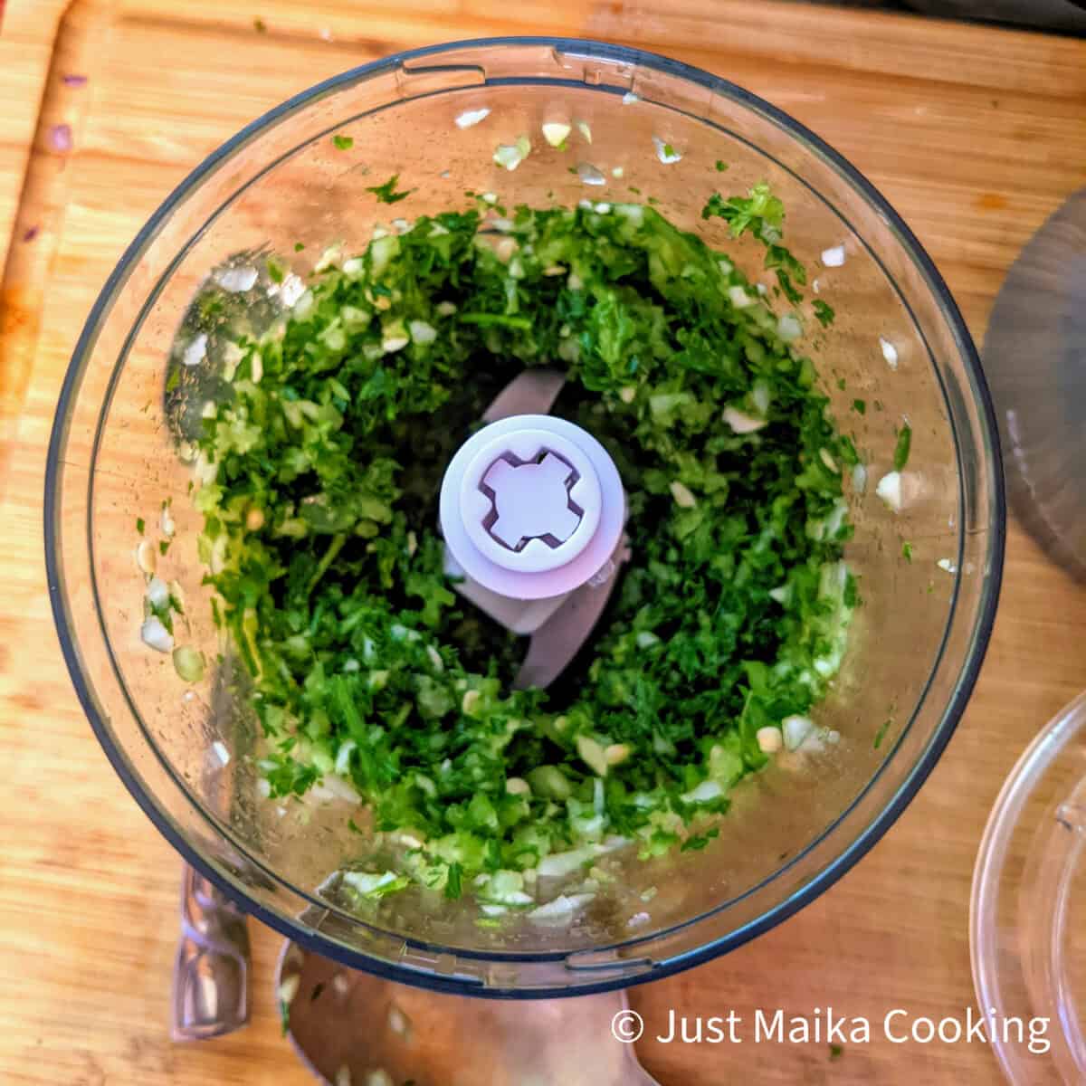 chopped green seasoning in the food processor container sitting on a wooden cutting board