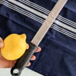 a hand holding a zester and lemon