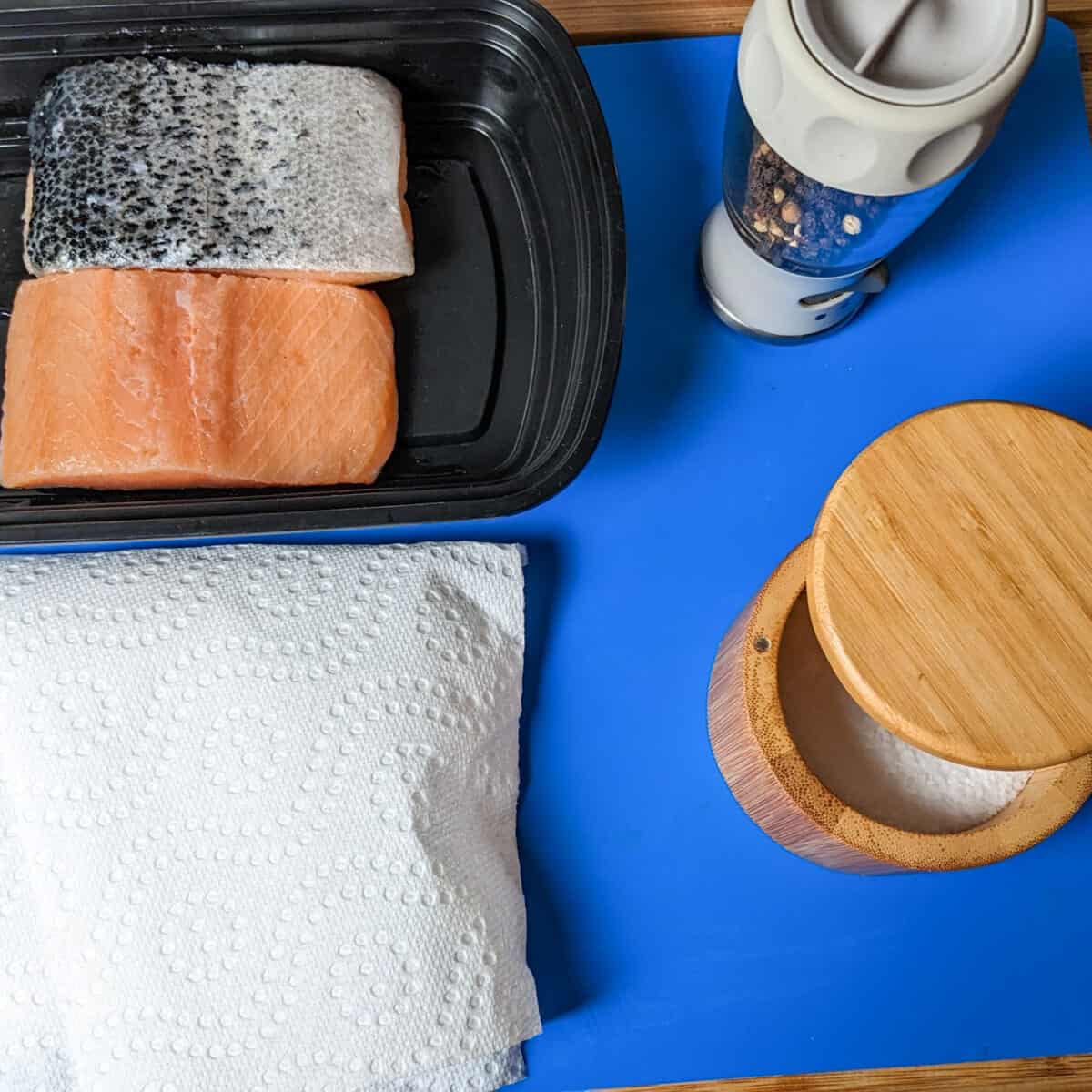 Fresh salmon fillets, kitchen essentials, and spices arranged for meal preparation on a blue surface.