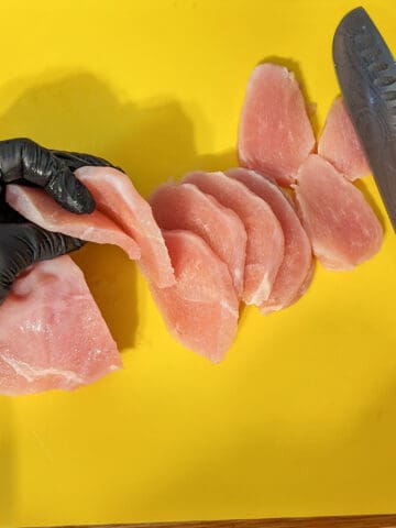 half thawed frozen chicken sliced on a cutting board for perfect slices.