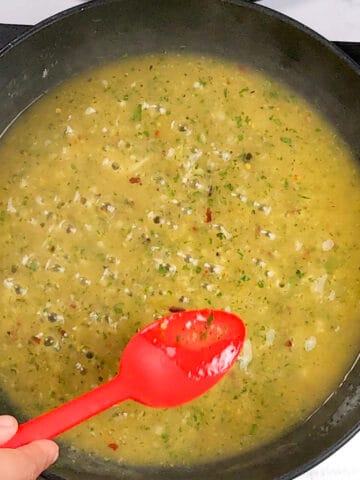 the wet lemon pepper sauce reducing with small bubbles in a non-stick frying pan being tasted with a silicone red spoon