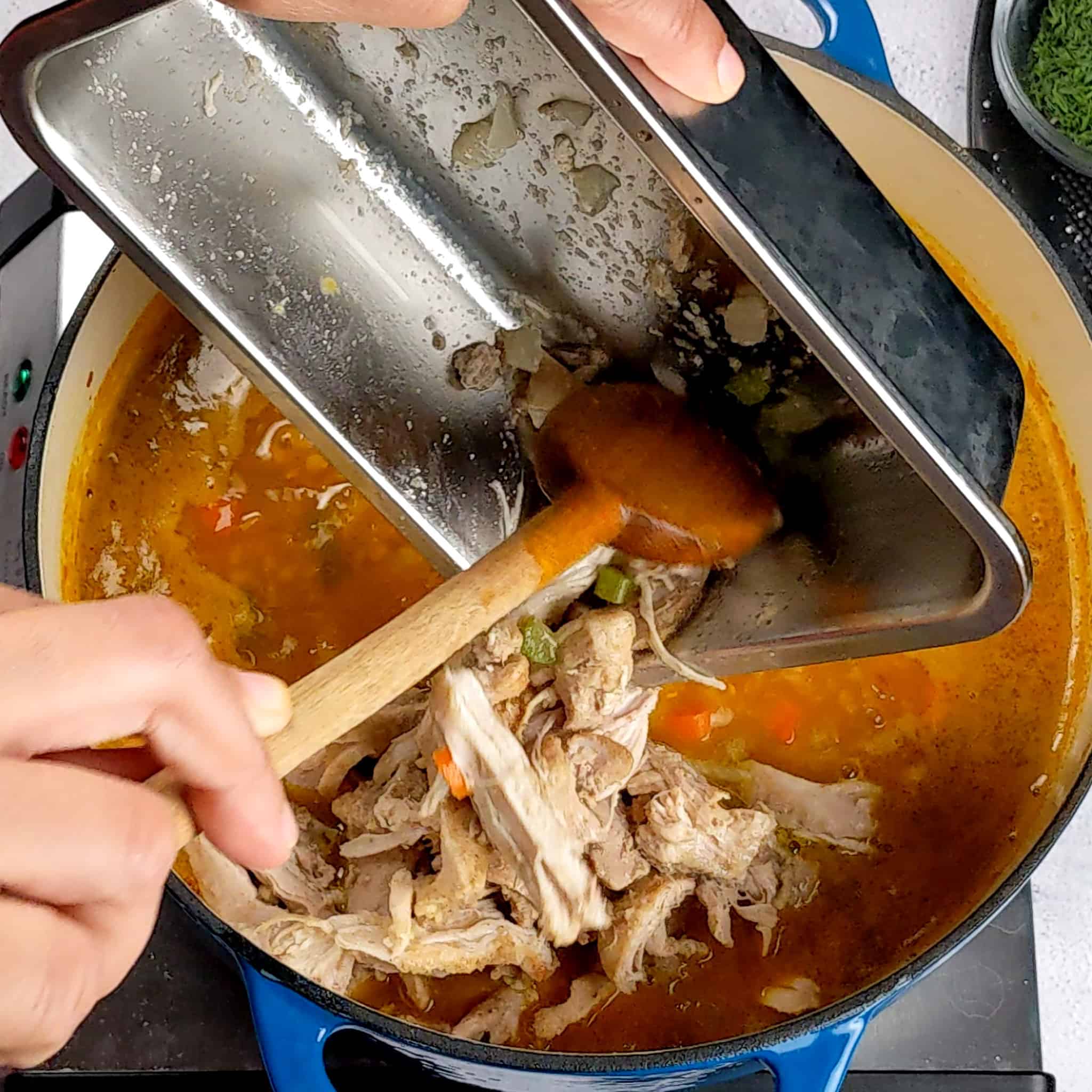 shredded chicken being spoon back into the pot with a wooden spoon