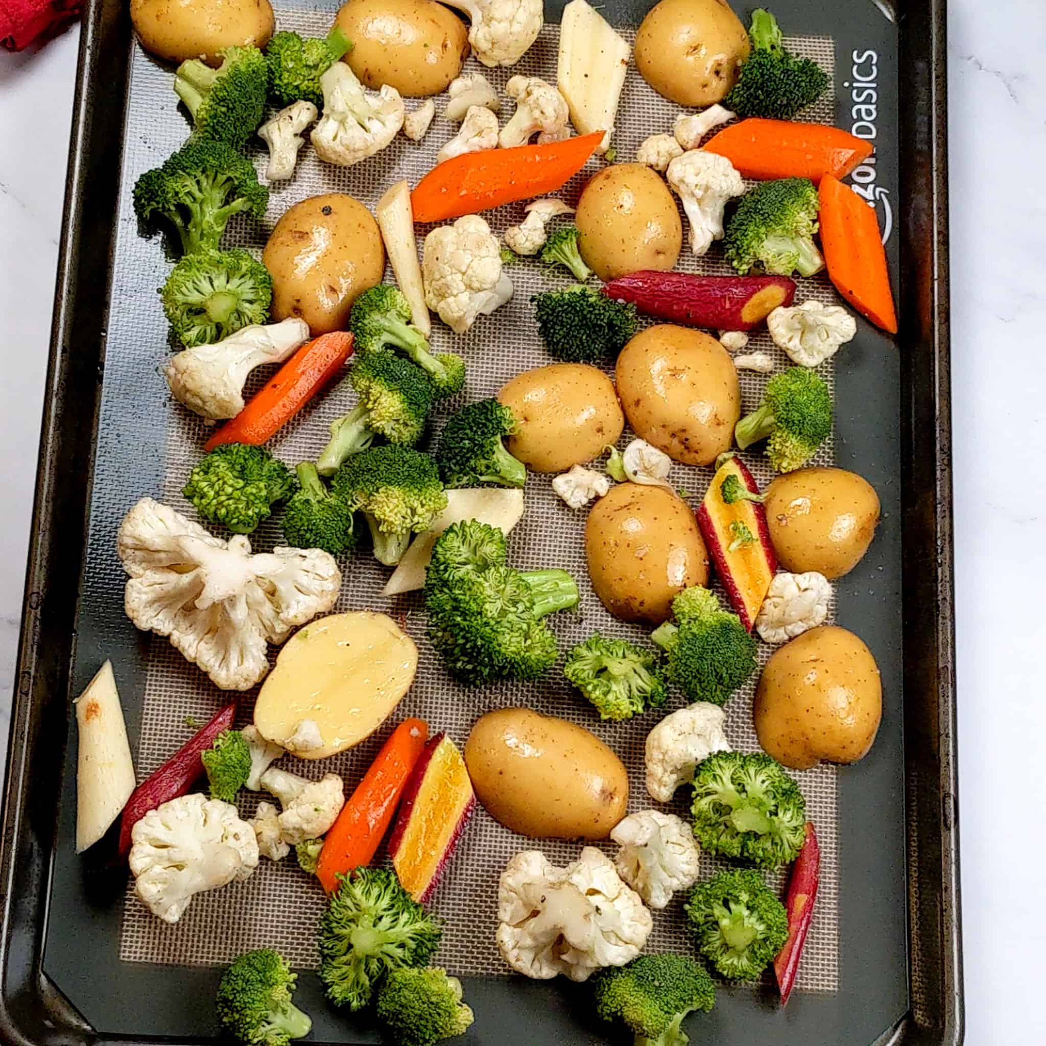 salt and pepper seasoned mixed vegetables of baby Dutch potatoes, tri-color carrots, broccoli and cauliflower florets on a non-stick baking liner layered sheet pan.