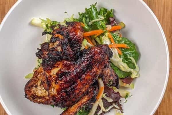 top view the Crispy Air Fryer Honey Jerk Rubbed Chicken Wings recipe next to marinated vegetables with greens and vinaigrette in a wide rim bowl