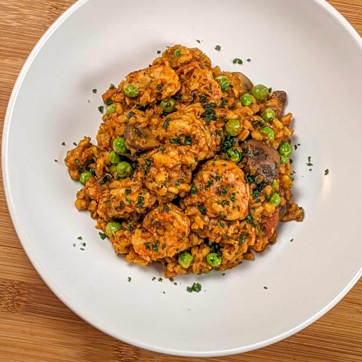 The Spicy Shrimp Farro Risotto with Mushrooms and Peas recipe in a wide rim bowl garnished with chopped parsley