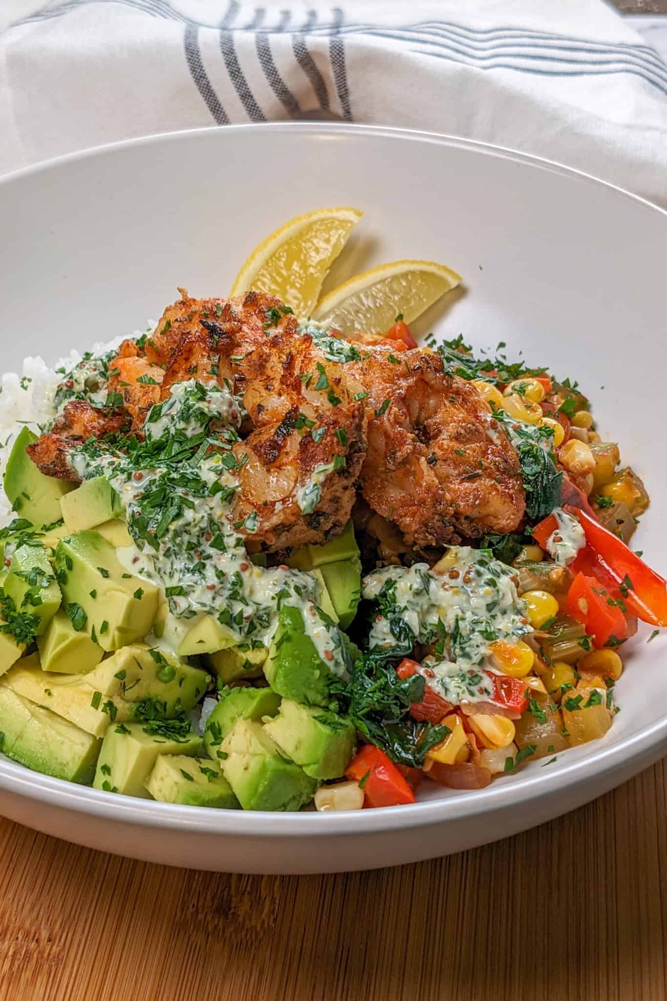 Side view of the Spicy Cajun Shrimp Rice Bowl with Lemon Remoulade in a wide rim bowl with diced avocado and lemon wedges.