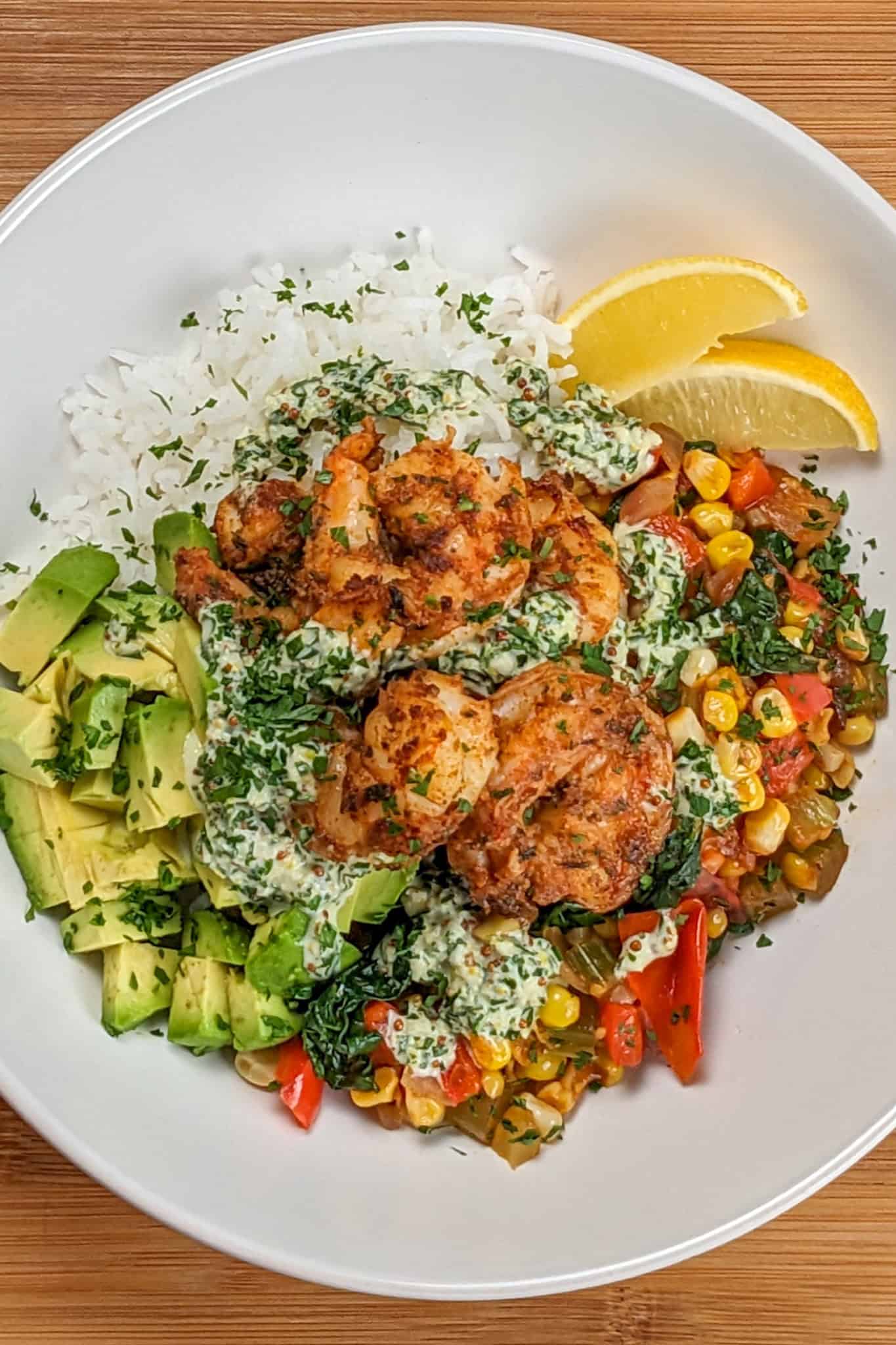 Top view of the Spicy Cajun Shrimp Rice Bowl with Lemon Remoulade in a wide rim bowl with diced avocado and lemon wedges.