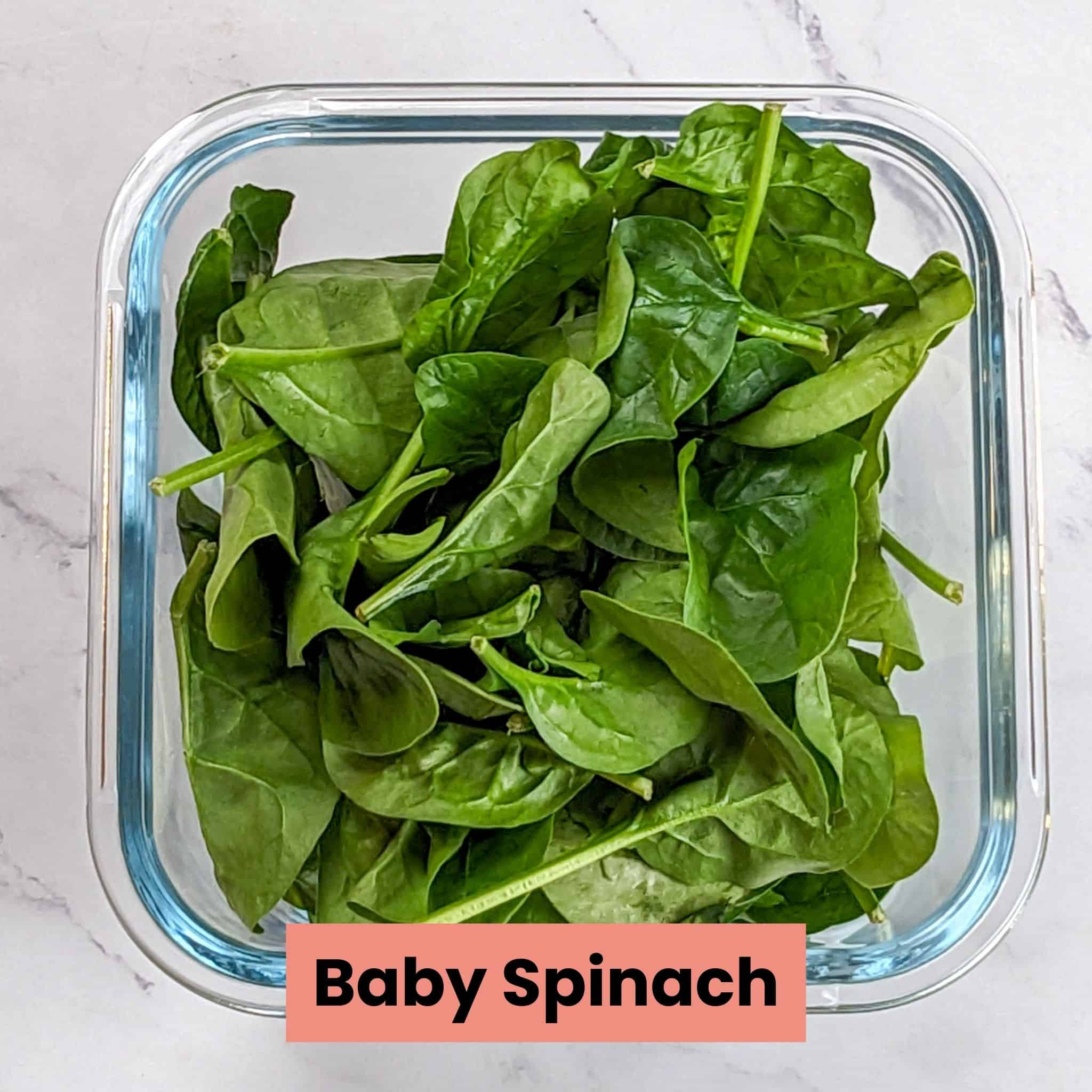 fresh raw baby spinach in a glass square container.
