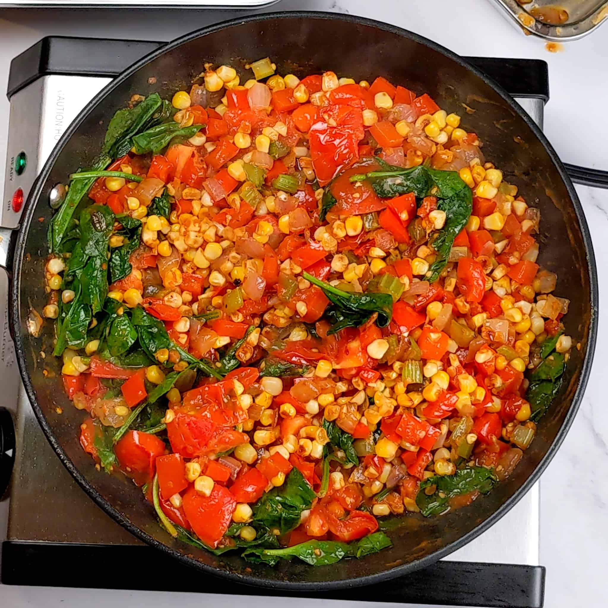 the cooked vegetables medley of corn, red bell pepper, red onion, celery and baby spinach in a skillet.