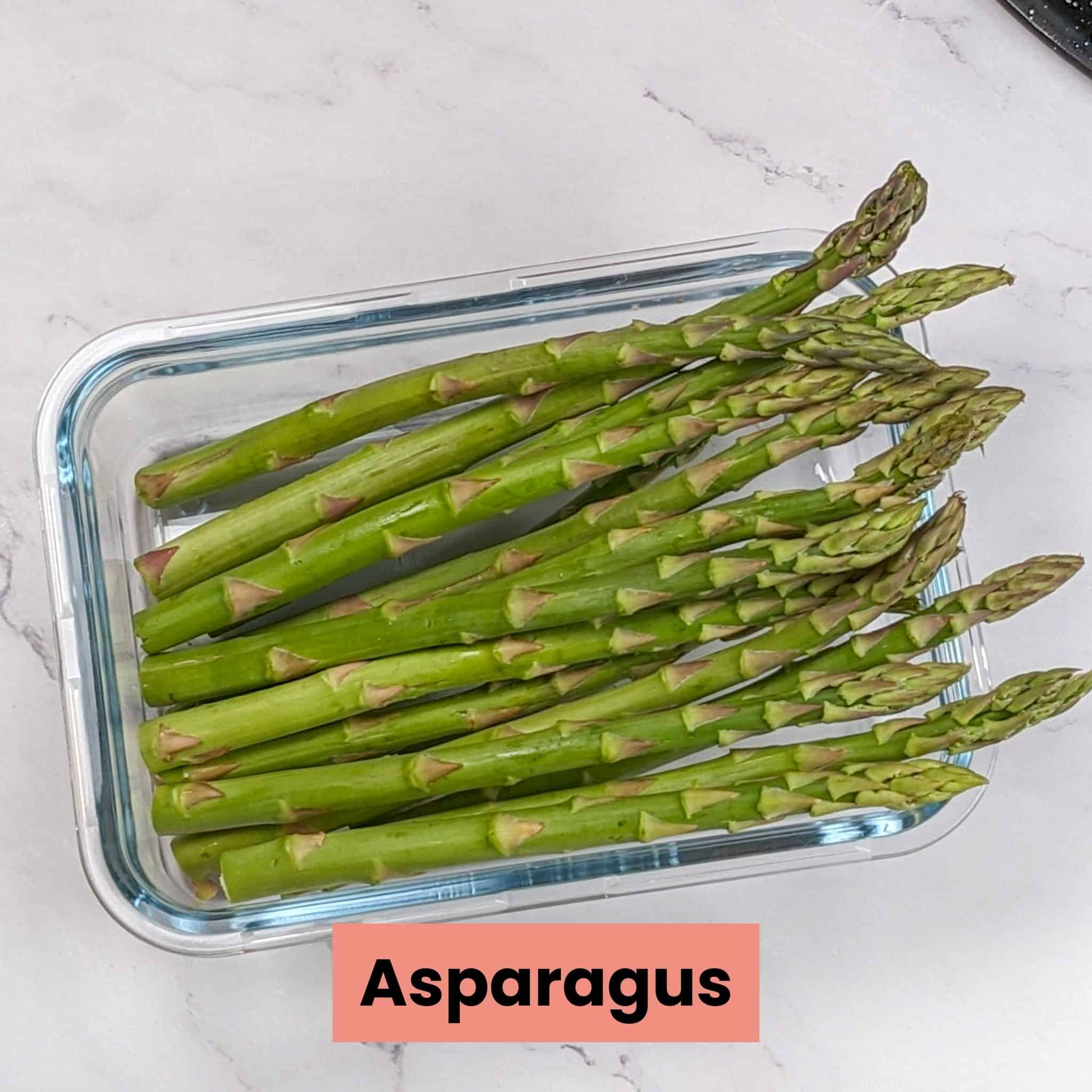large asparagus with the bottoms trimmed in a glass rectangle container.