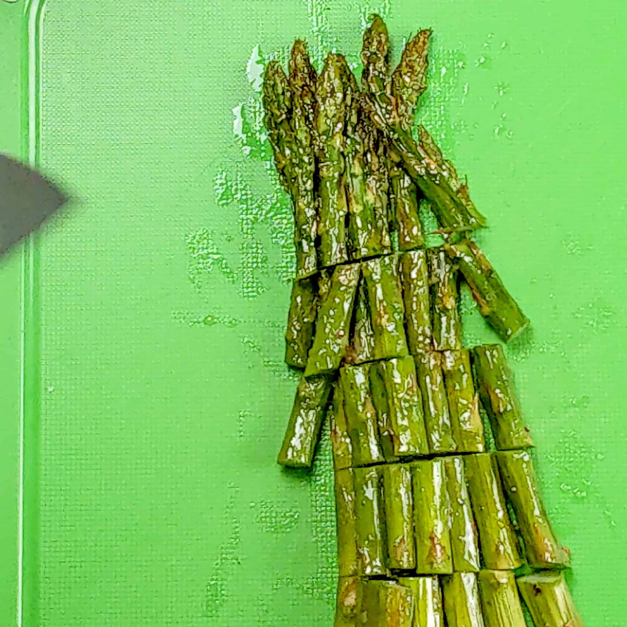 baked asparagus cut into 1-inch pieces on a plastic cutting board.