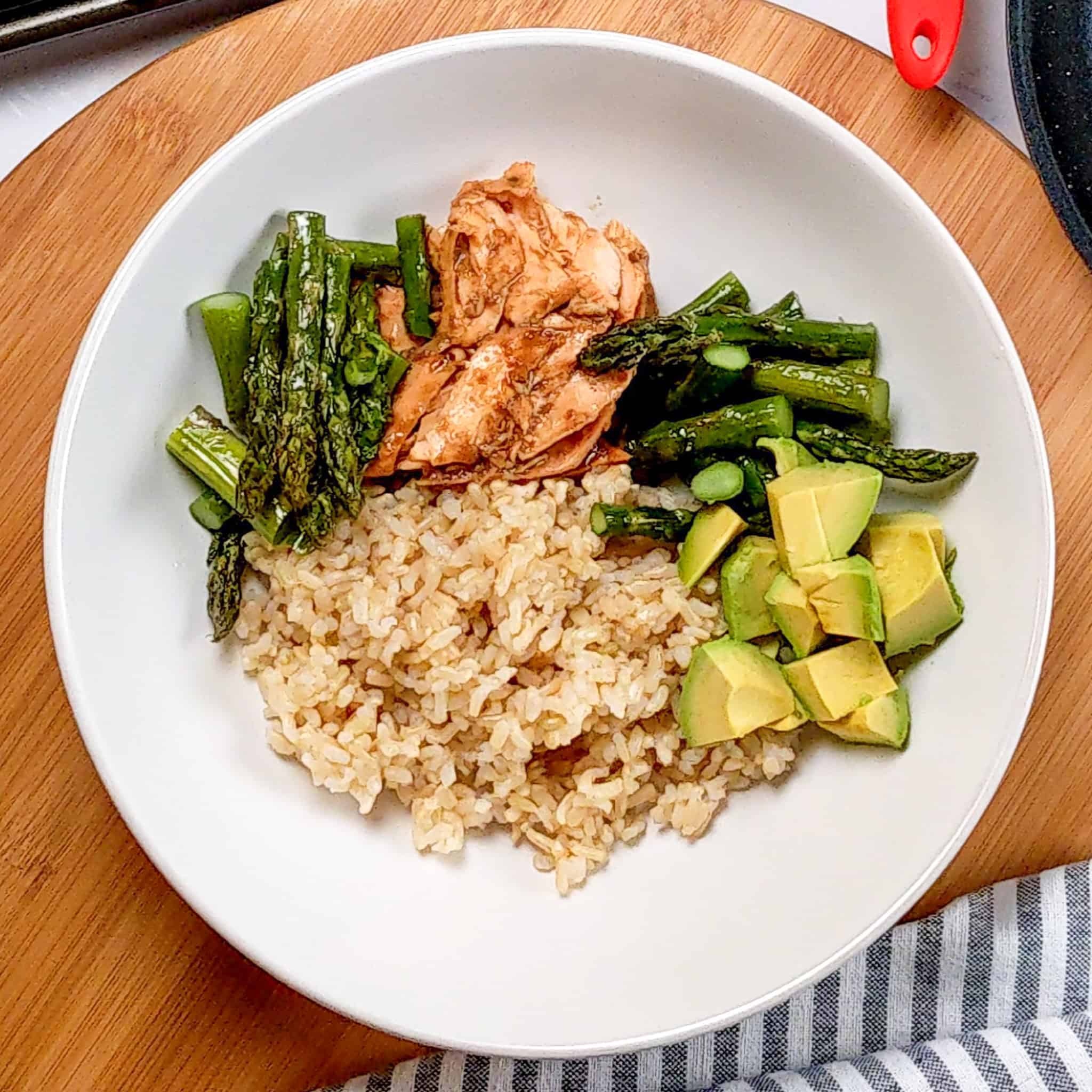 flaked miso salmon, asparagus, avocado chunks and brown rice assembled in a wide rim bowl.
