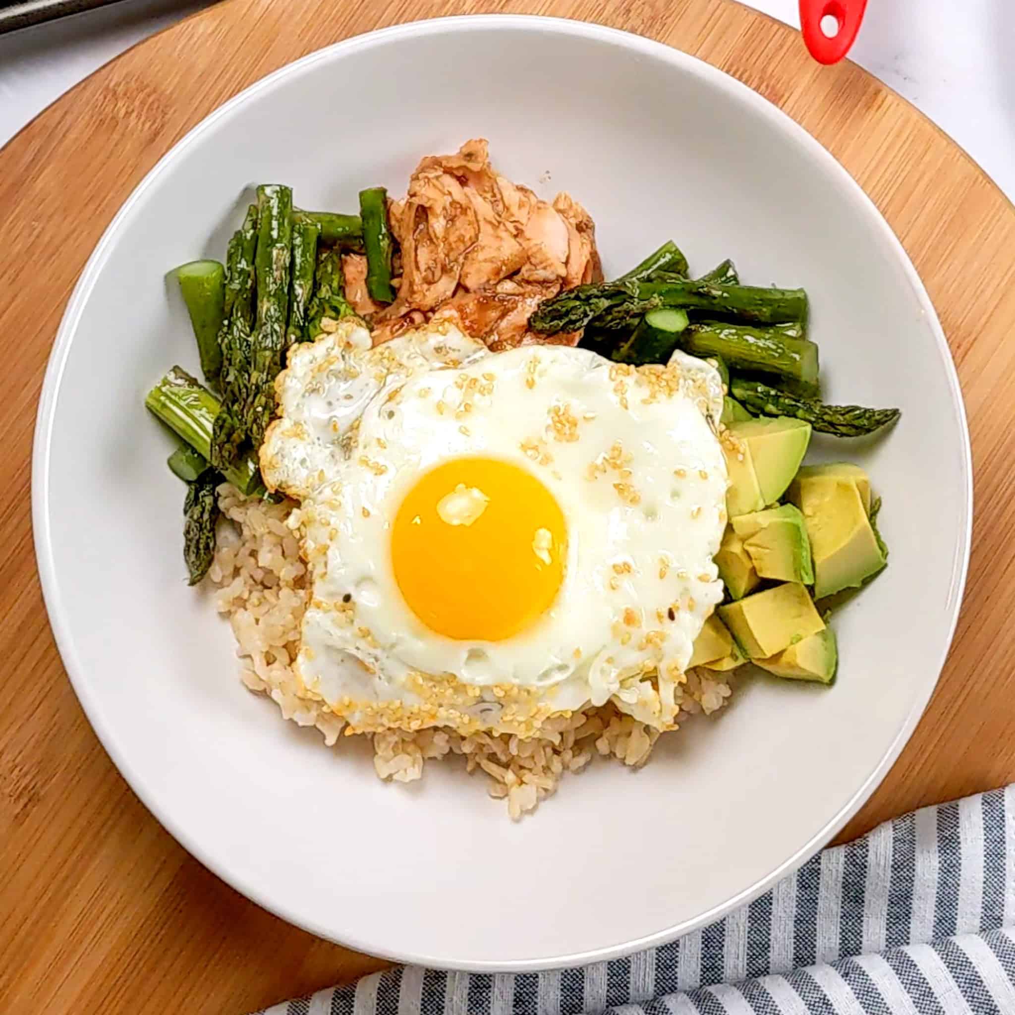 flaked miso salmon, asparagus, avocado chunks and brown rice assembled in a wide rim bowl with an egg on top.