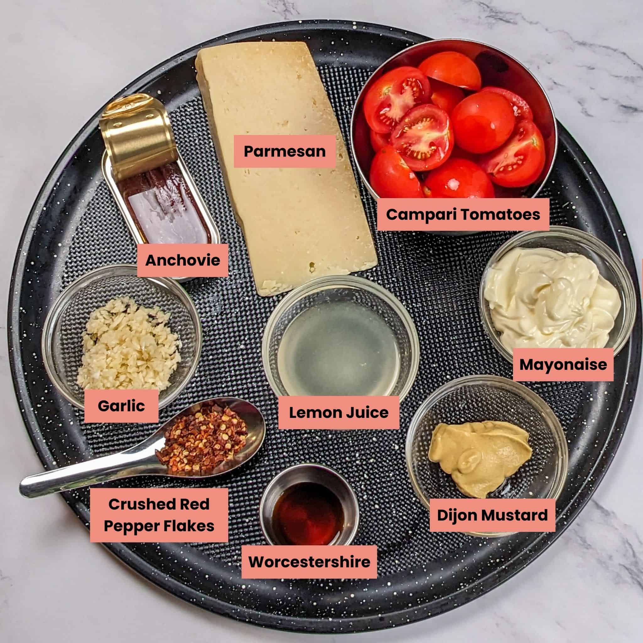 ingredients for the Caesar Salad with Egg Tomatoes and Chili-Infused Croutons in containers on a large round pizza pan.