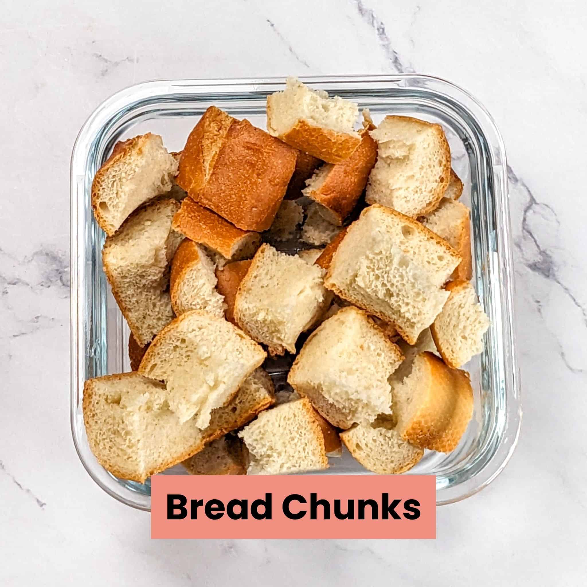 bread torn into chunks piled up in a glass square dish.