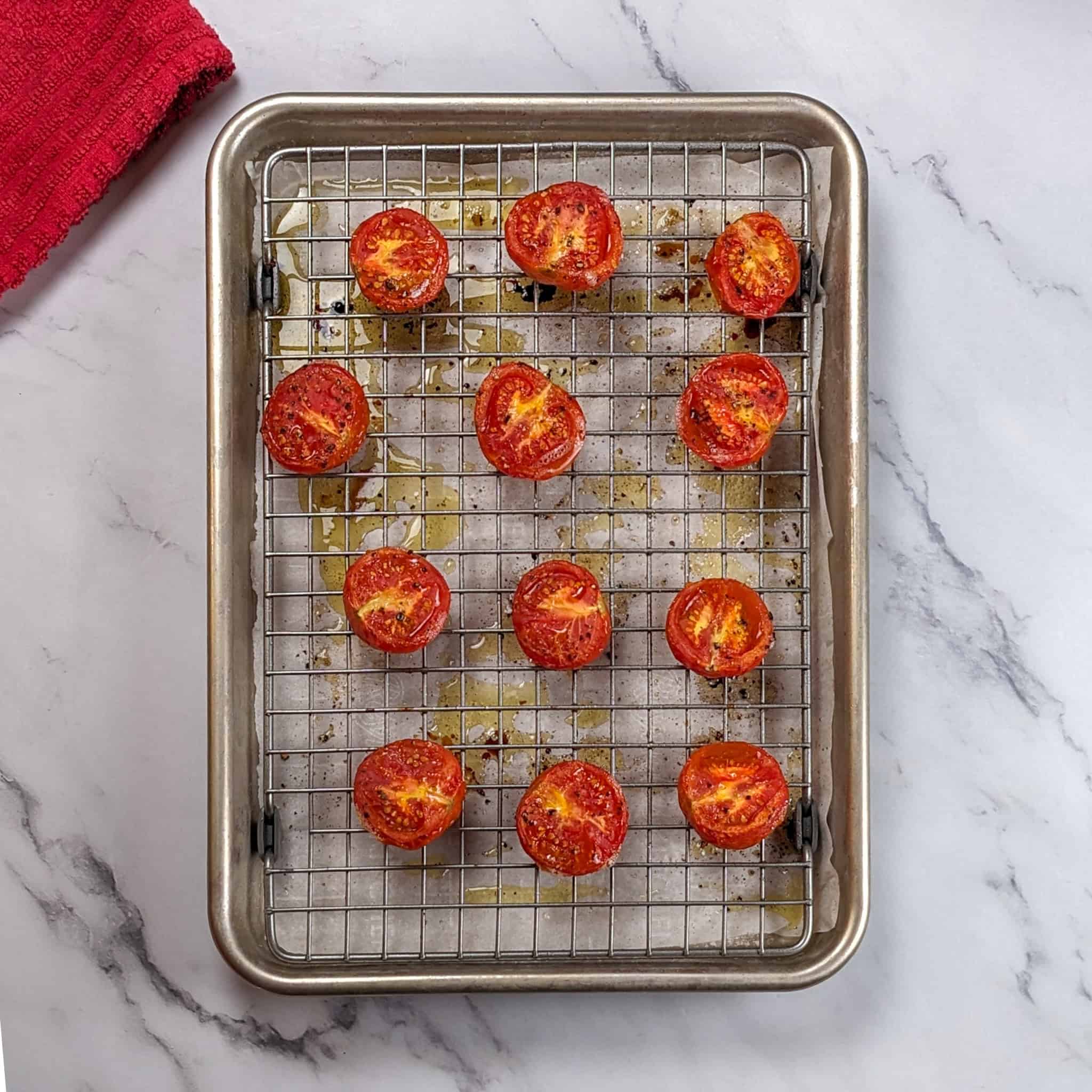 roasted halved campari tomatoes on a sheet pan and rack lined with parchment paper.