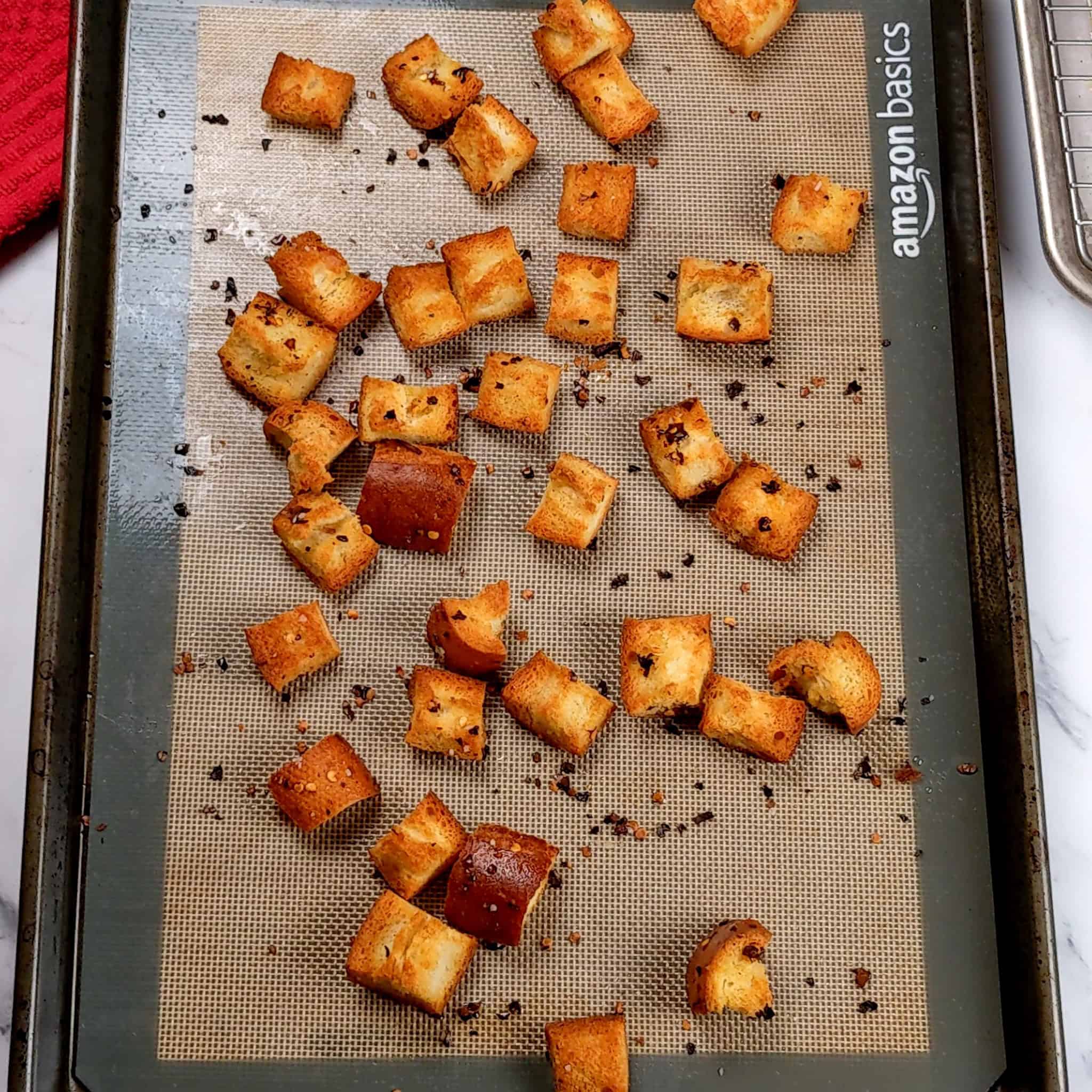 toasted croutons with red pepper chili flakes and olive oil on a silicone liner lined sheet pan.