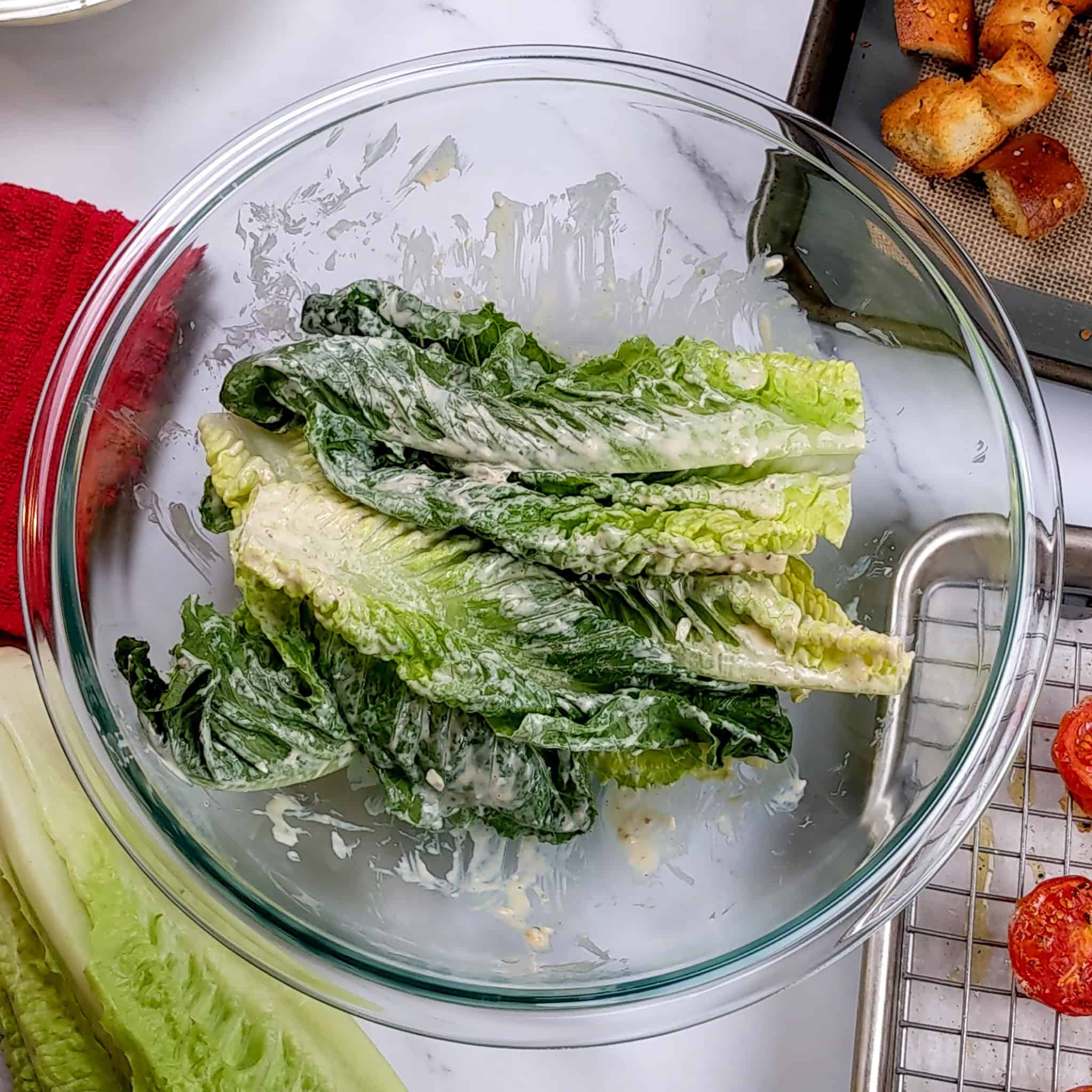 romaine leaves tossed in Caesar salad dressing in a glass mixing bowl.