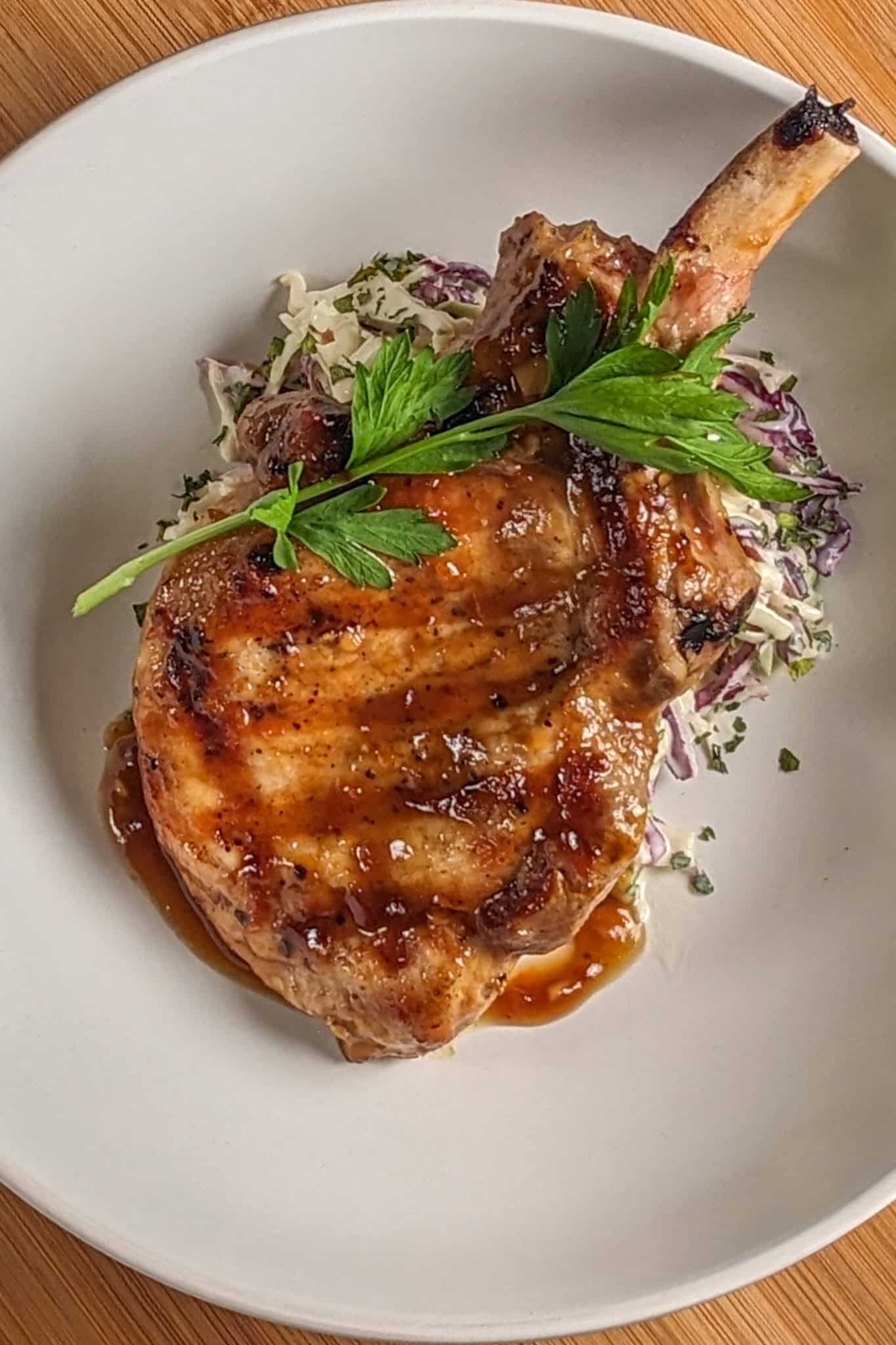 habanero tamarind glazed pork chop on a bed of deli-style coleslaw on a wide rim bowl.