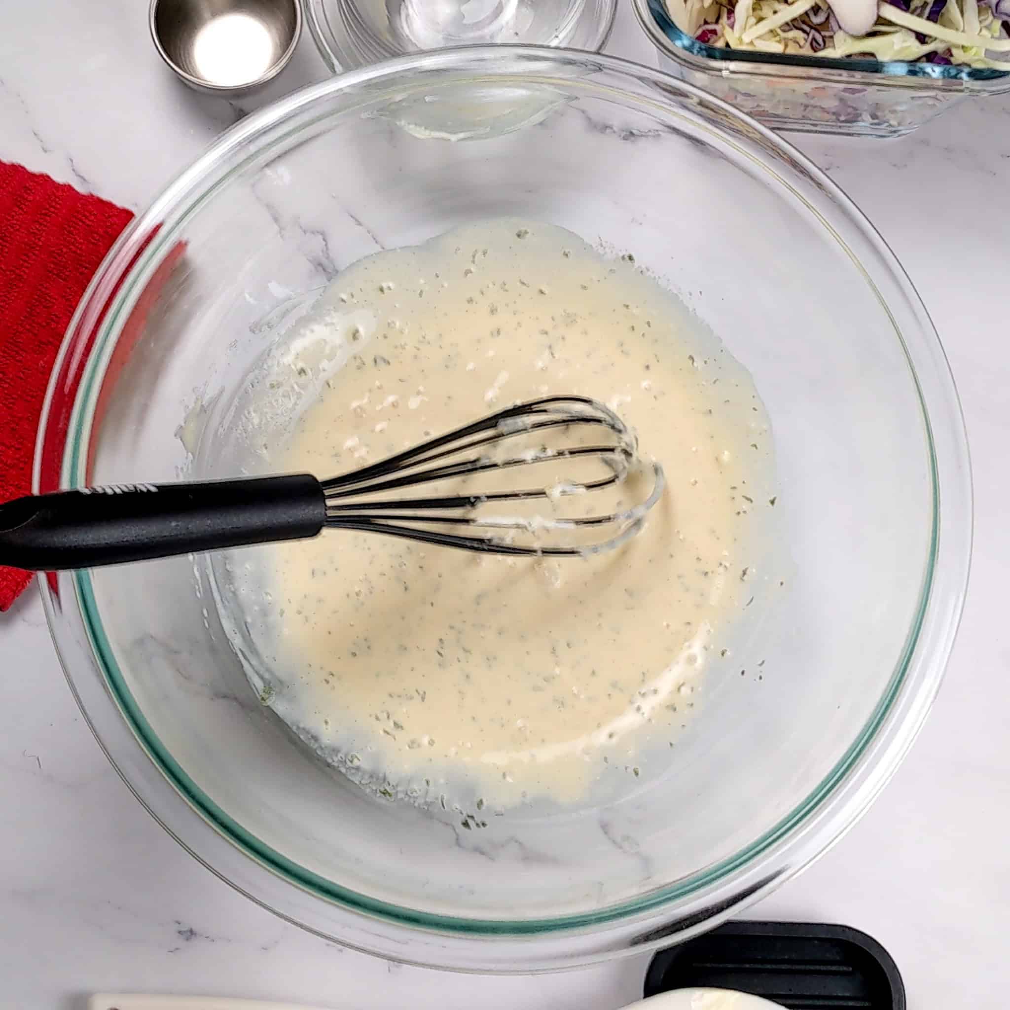 homemade coleslaw dressing in a glass mixing bowl with a silicone whisk.