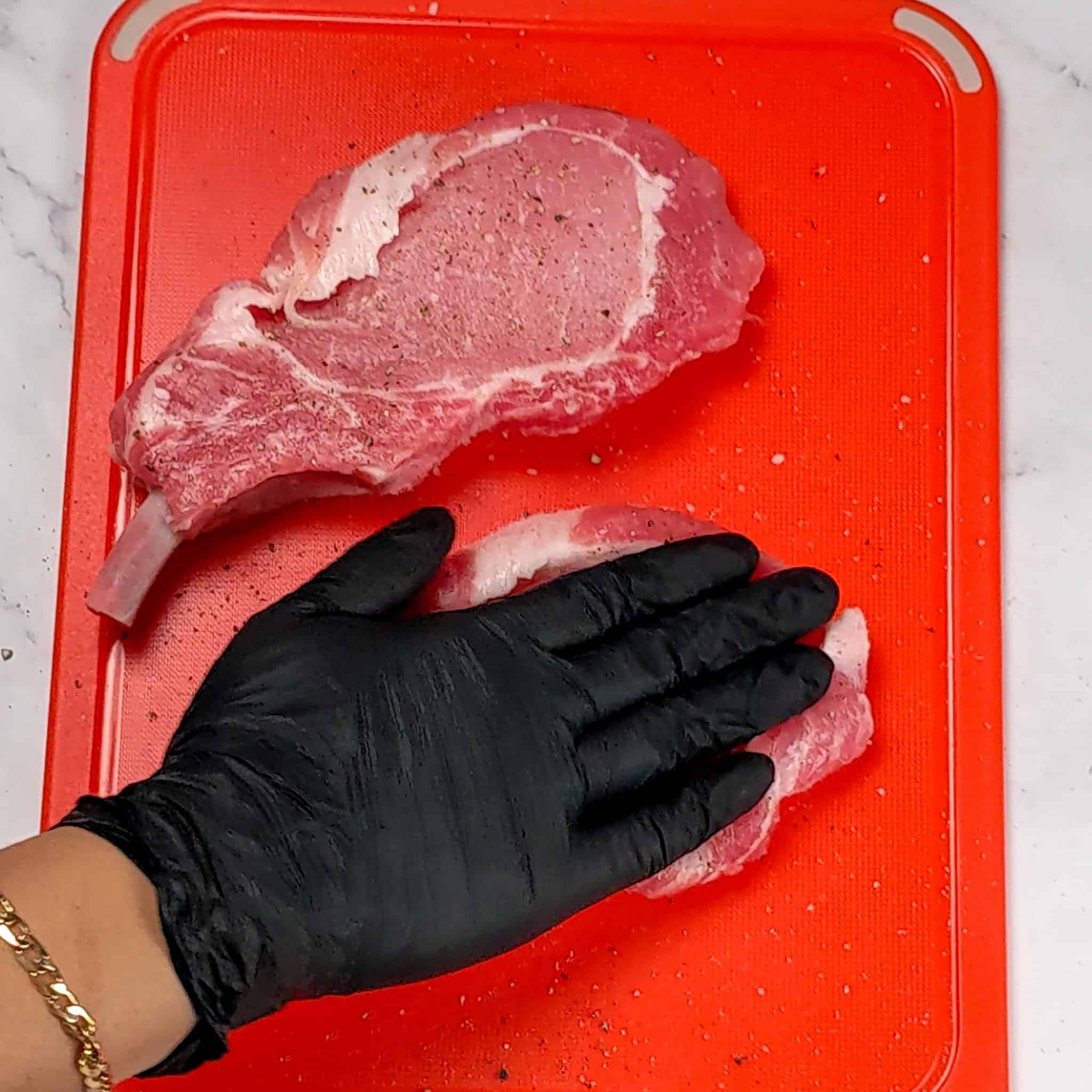 salt and pepper seasoned rib pork chops being pressed with a gloved hand.