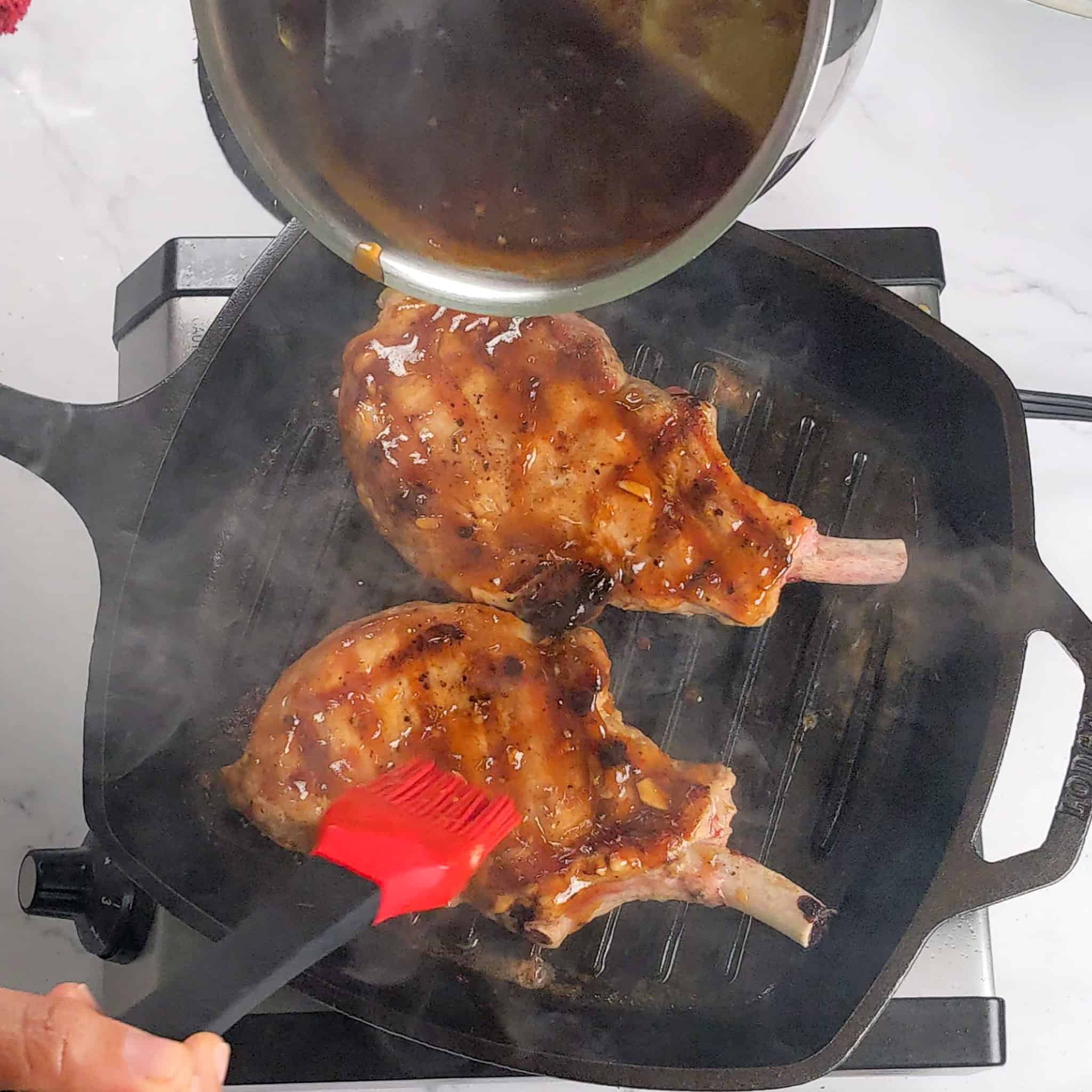 grilled pork chops in a grill pan being brushed with the tamarind habanero glaze.