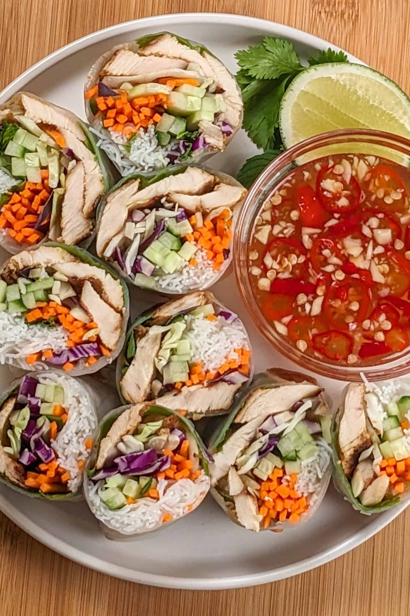 sliced lemongrass chicken, cabbage, rice vermicelli spring roll with nouc cham sauce on side all on a round flat plate.