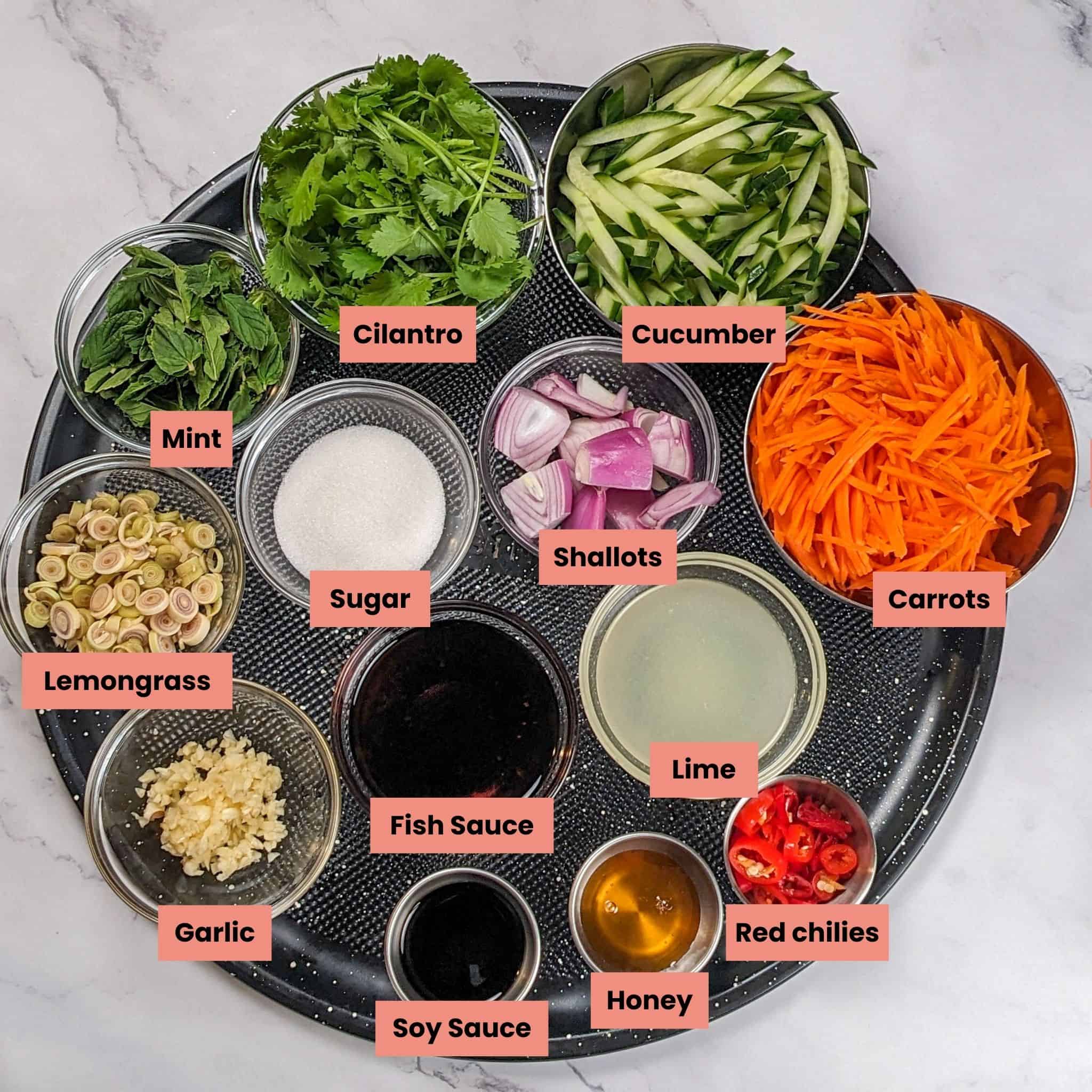 Ingredients for the Lemongrass Marinated Grilled Chicken Spring Rolls in containers on a large round pizza pan.