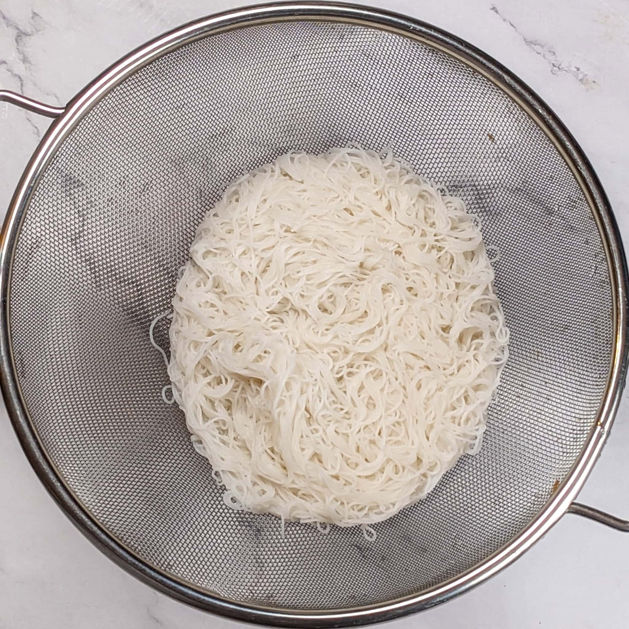 cooked and cooled rice vermicelli noodles in a sieve.