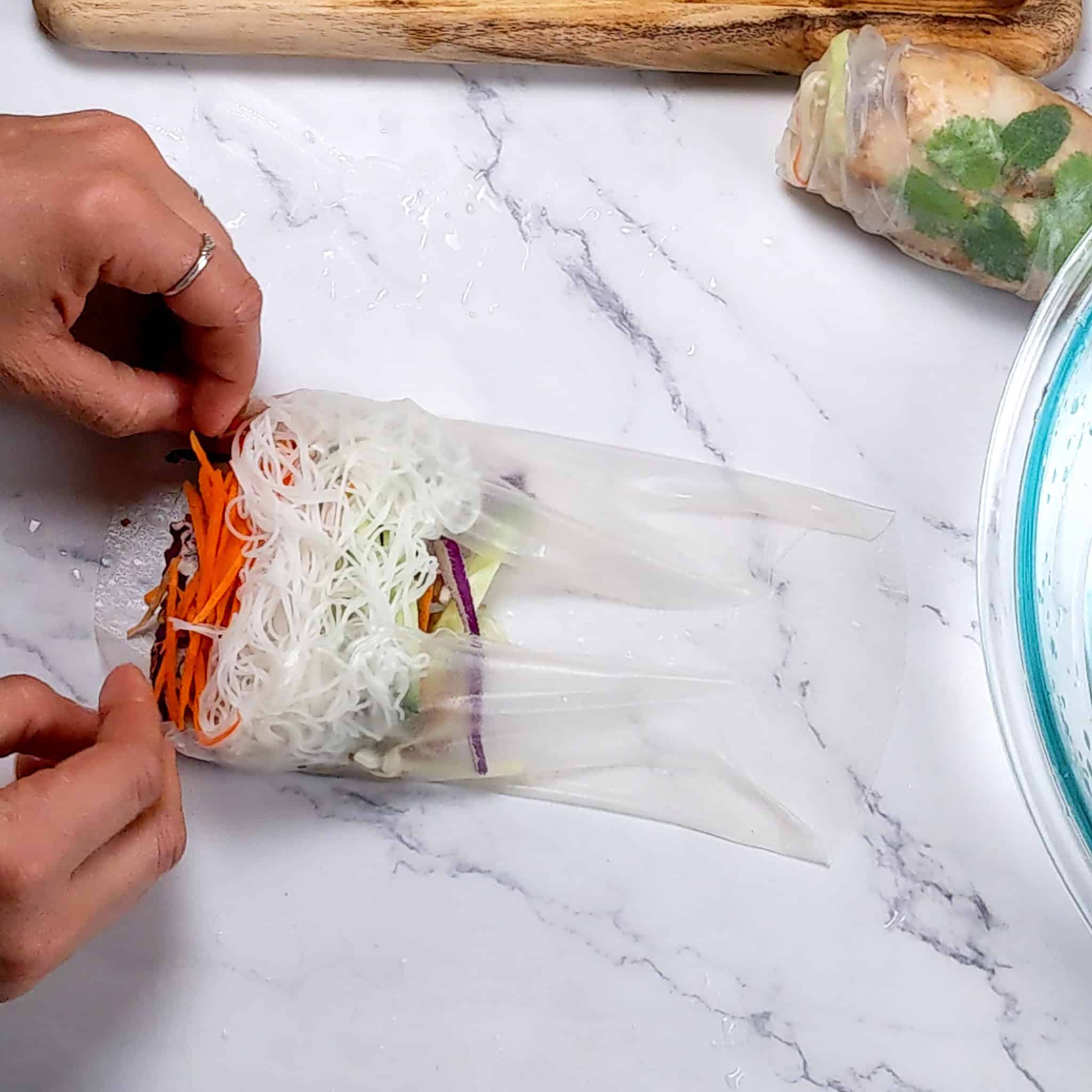 both sides of the rice paper roll folded in and two hands positioned to complete the roll.