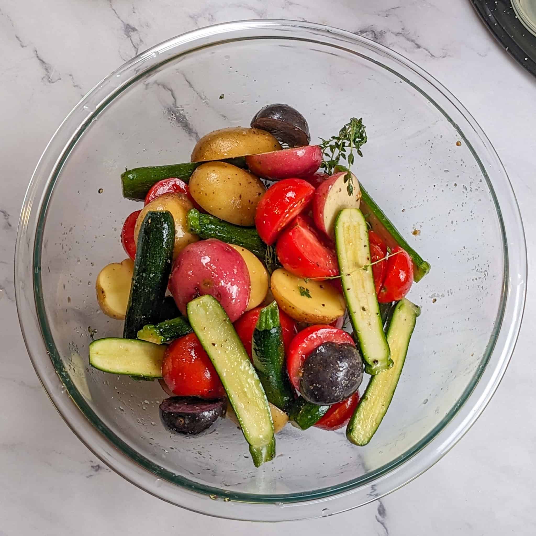 olive oil, fresh thyme, salt and cracked black pepper seasoned baby vegetables of halved baby zucchini, different color baby potatoes, and campari tomatoes in a large pyrex glass mixing bowl.