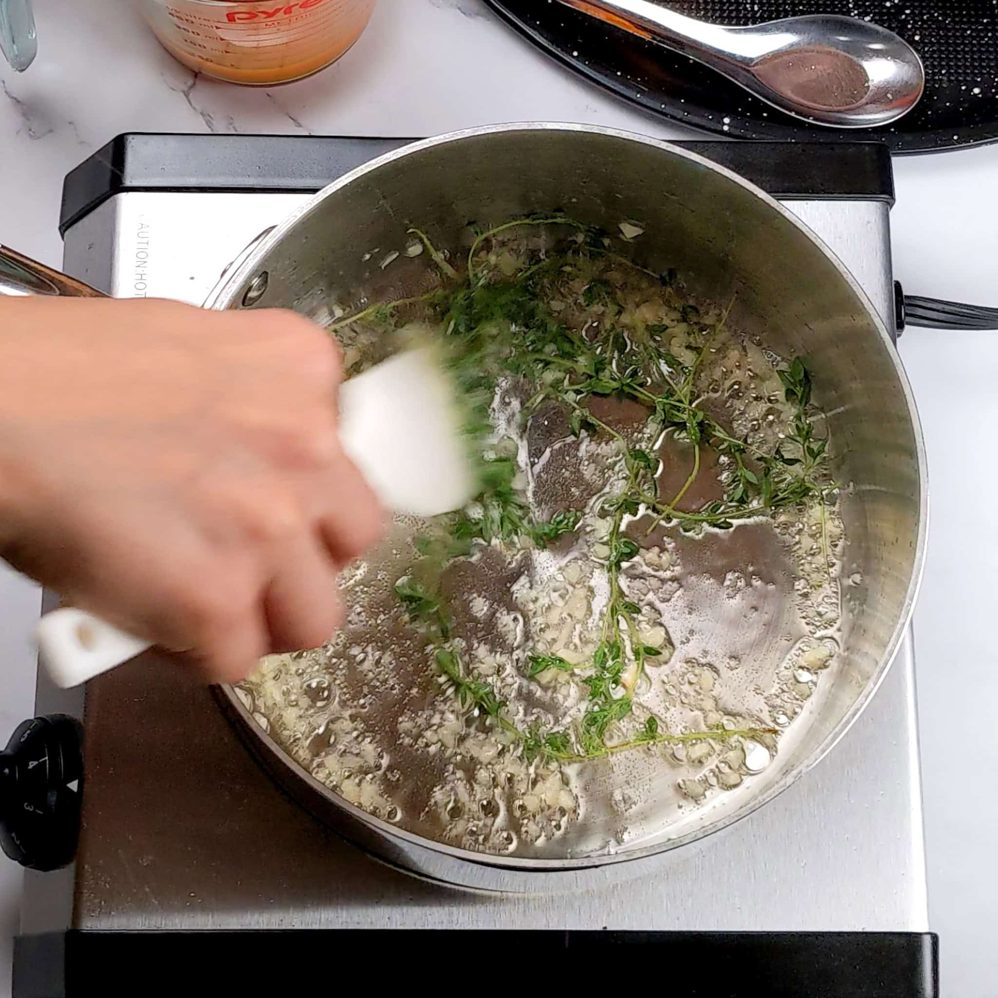 minced garlic and fresh thyme sauted in a large sauce pot with a silicone spatula.