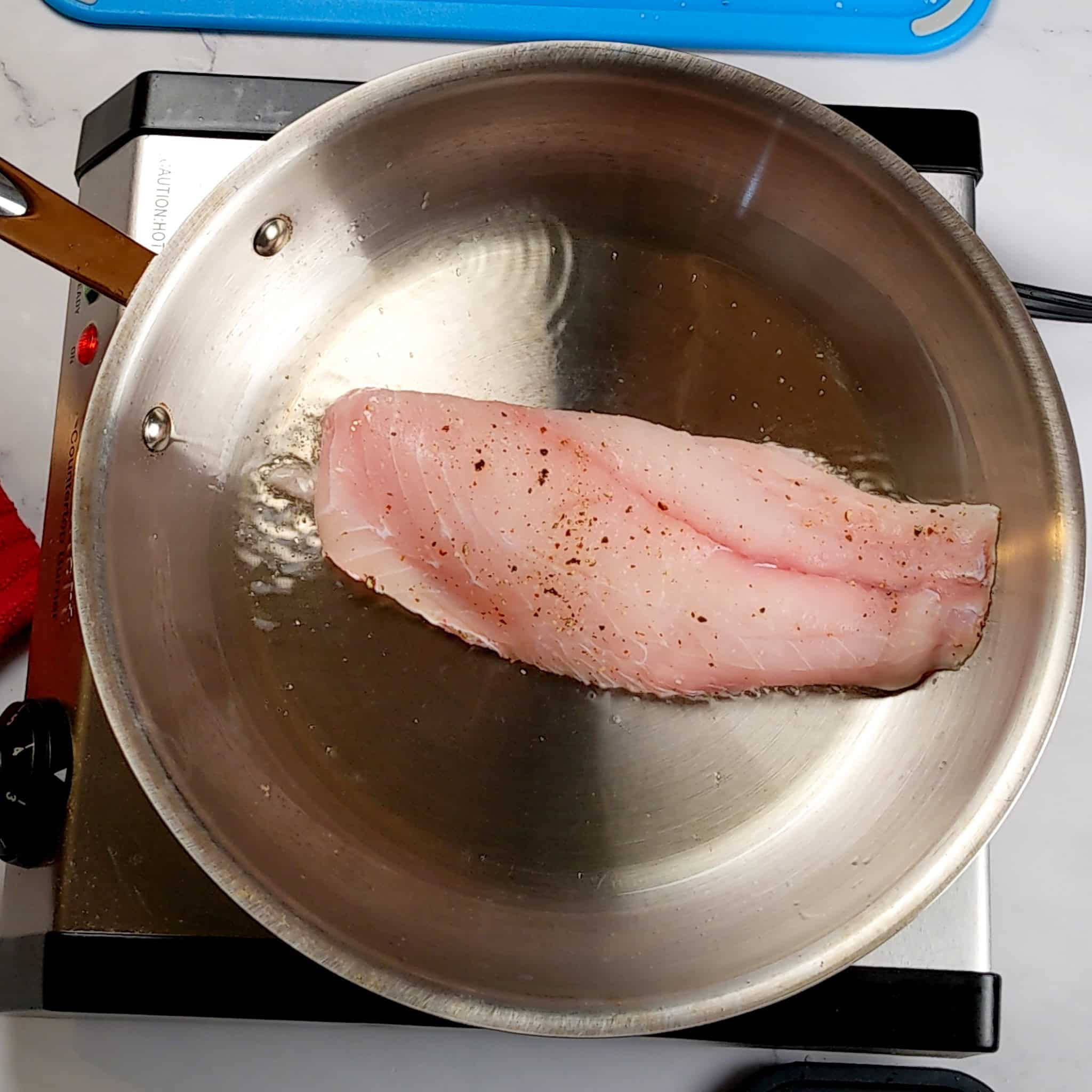 snapper filet skin side down frying in an stainless steel all clad frying pan.