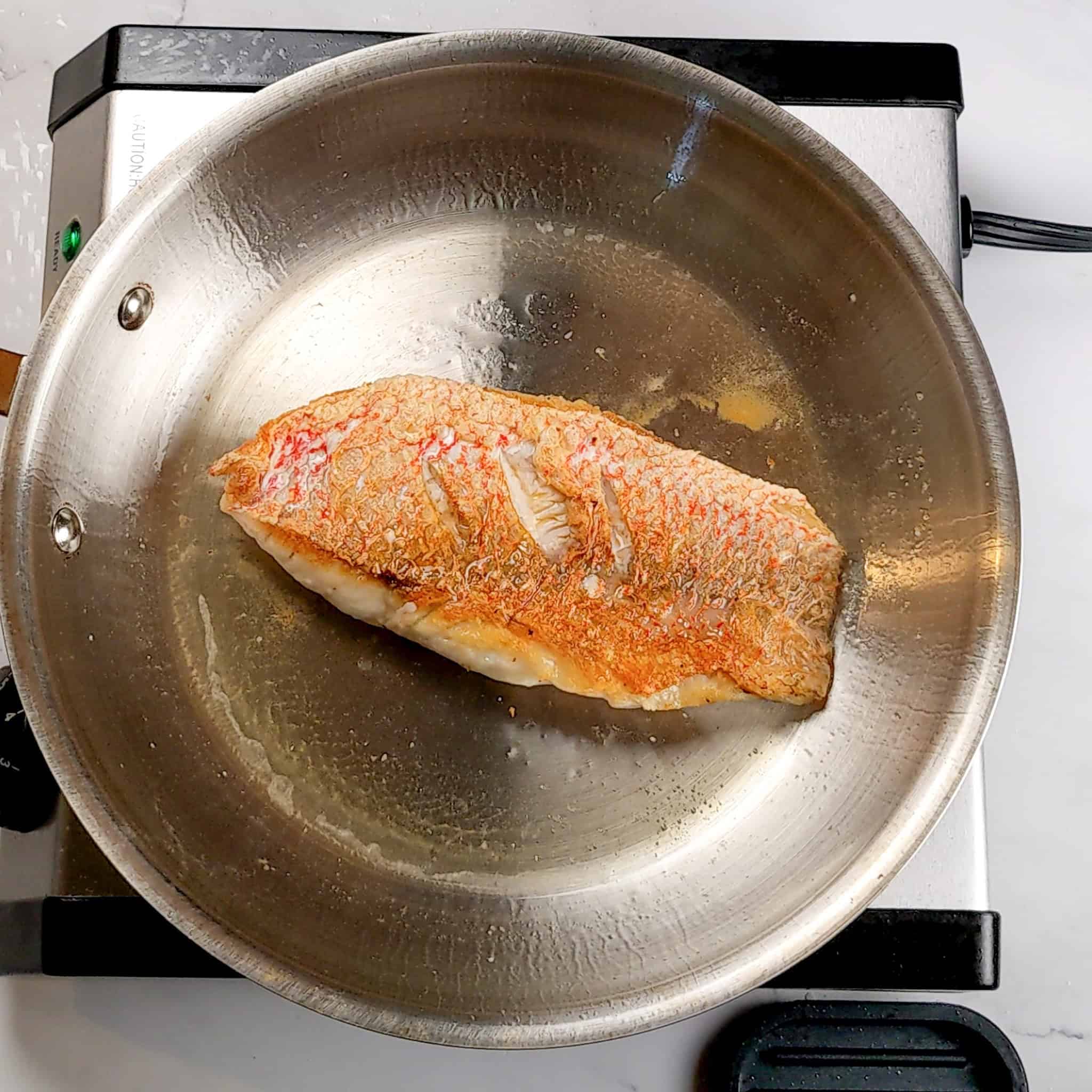 seared snapper fillet in a stainless steel frying pan.