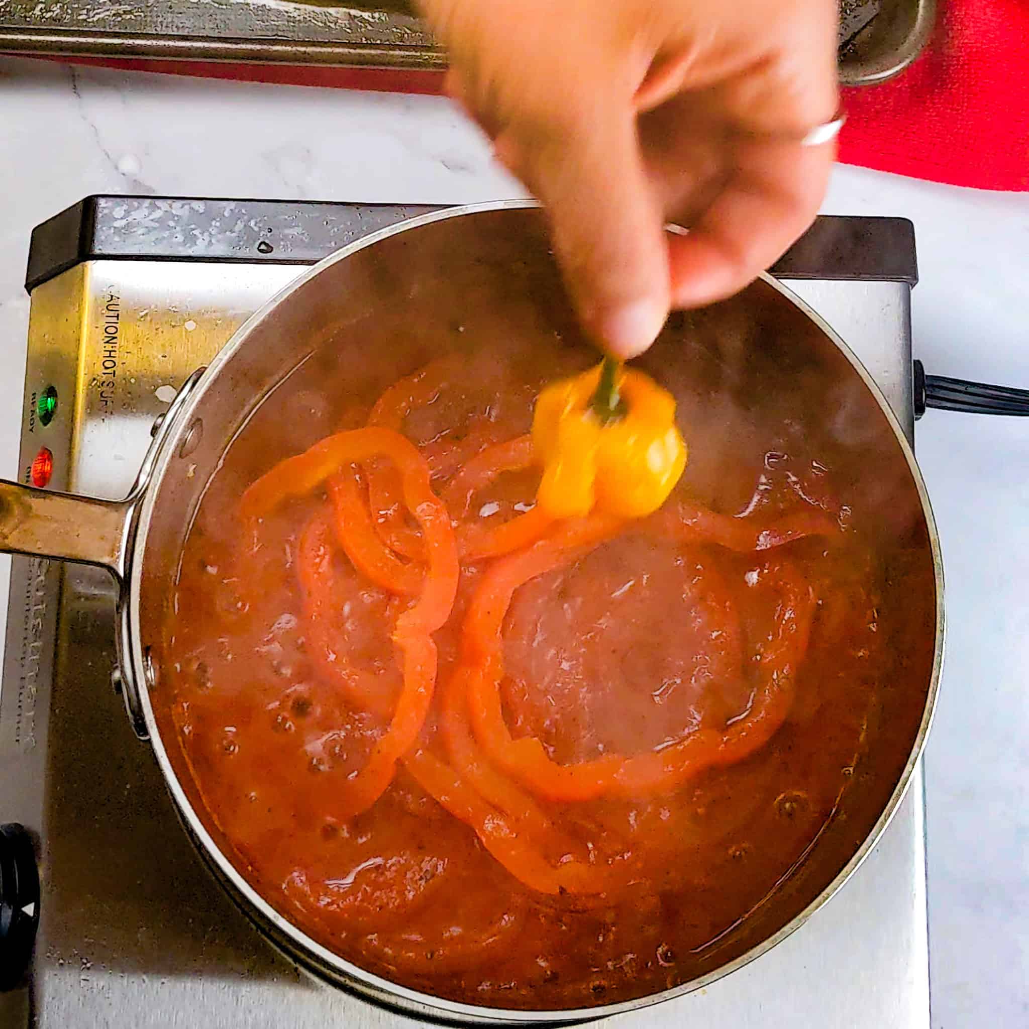 scotch bonnet pepper removed by a hand from the spicy creole sauce.