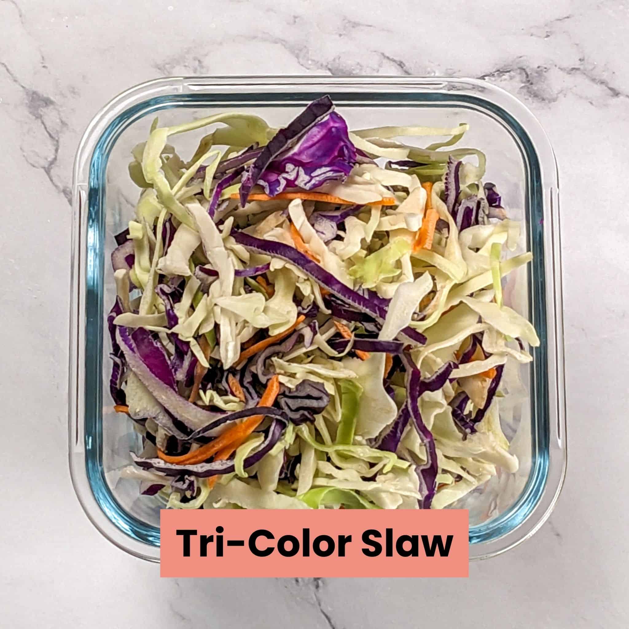 tri-color slaw of shredded green cabbage, red cabbage and carrots in a square glass deep container.