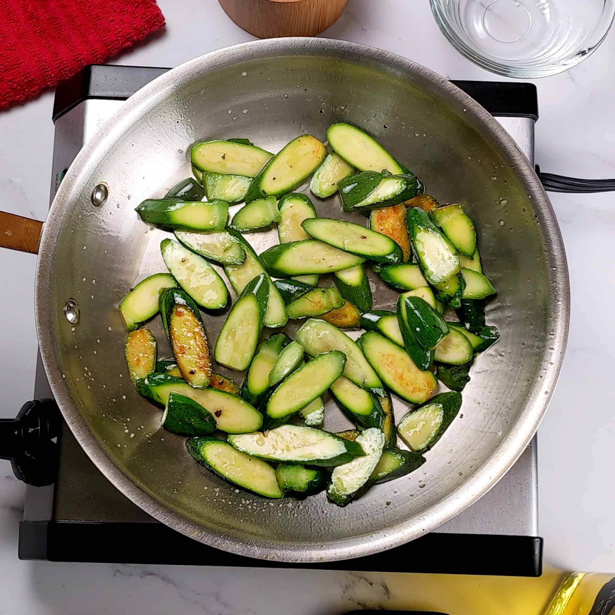 sliced baby zucchini sauteing in a stainless steel skillet.