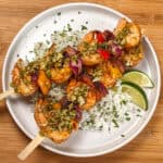two Grilled Shrimp skewers with Garlic Jalapeno Butter and Cilantro Lime Rice on a flat round plate garnished with lime wedges and chopped cilantro.