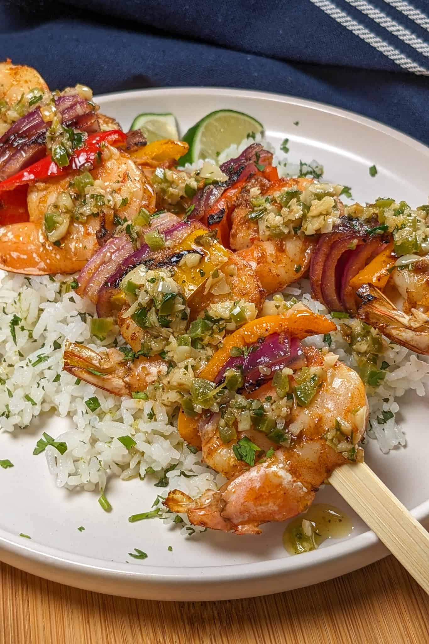 two Grilled Shrimp skewers with Garlic Jalapeno Butter and Cilantro Lime Rice on a flat round plate garnished with lime wedges and chopped cilantro.