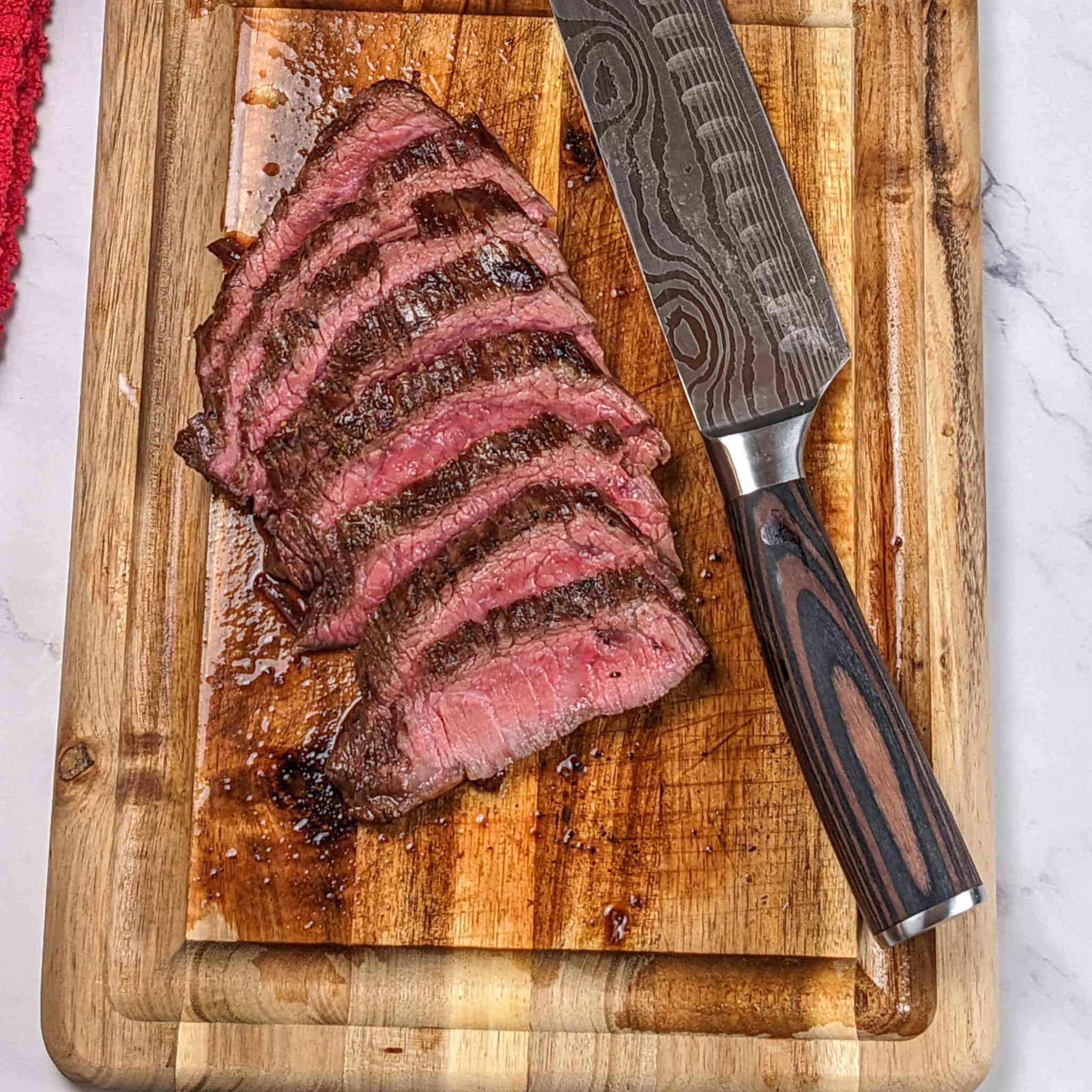 medium rare thinly sliced pan-grilled flank steak cascading on a mini wooden cutting board with a knife laying next to it.