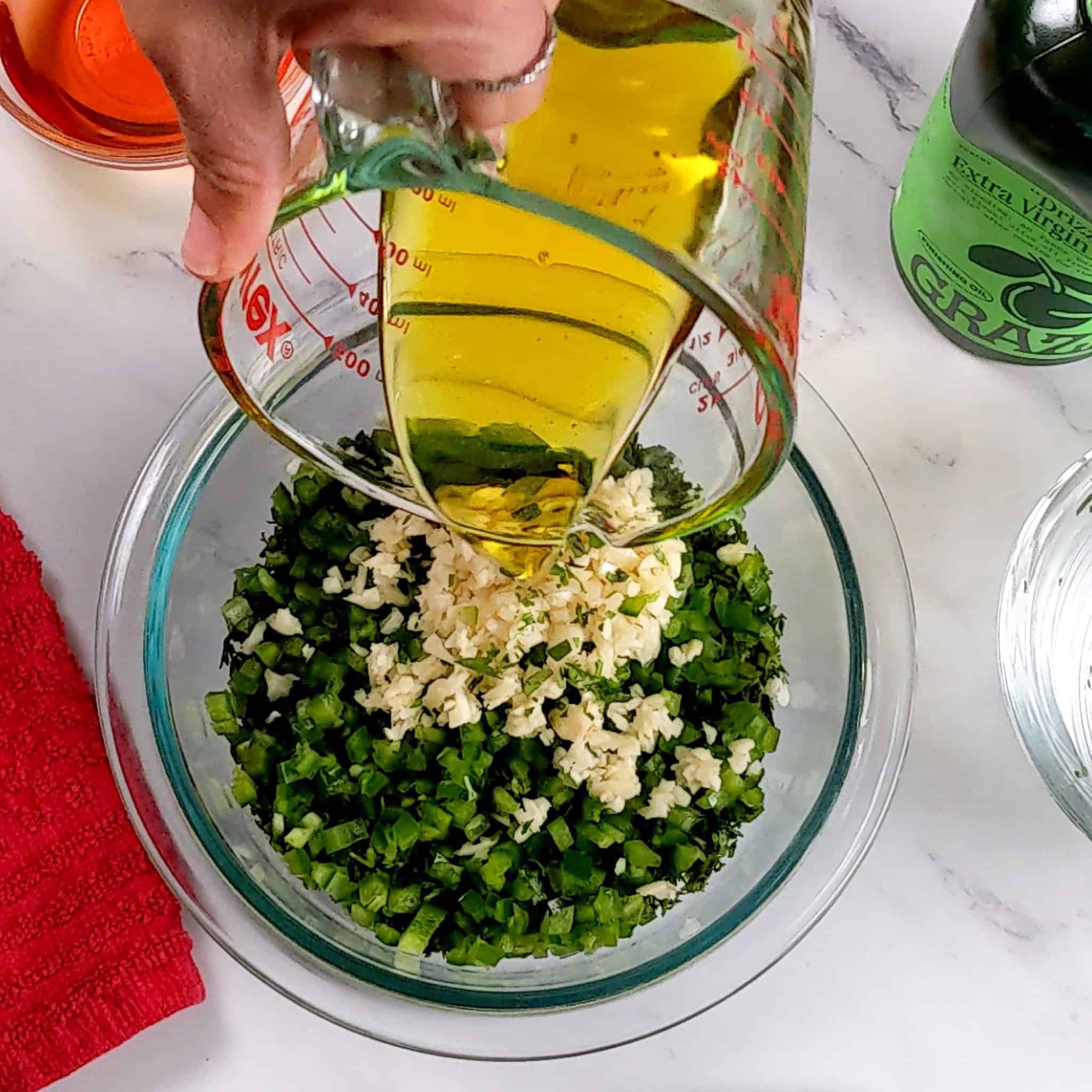 extra virgin olive oil being poured from a glass pyrex measuring cup into the ingredients to make chimichurri sauce.