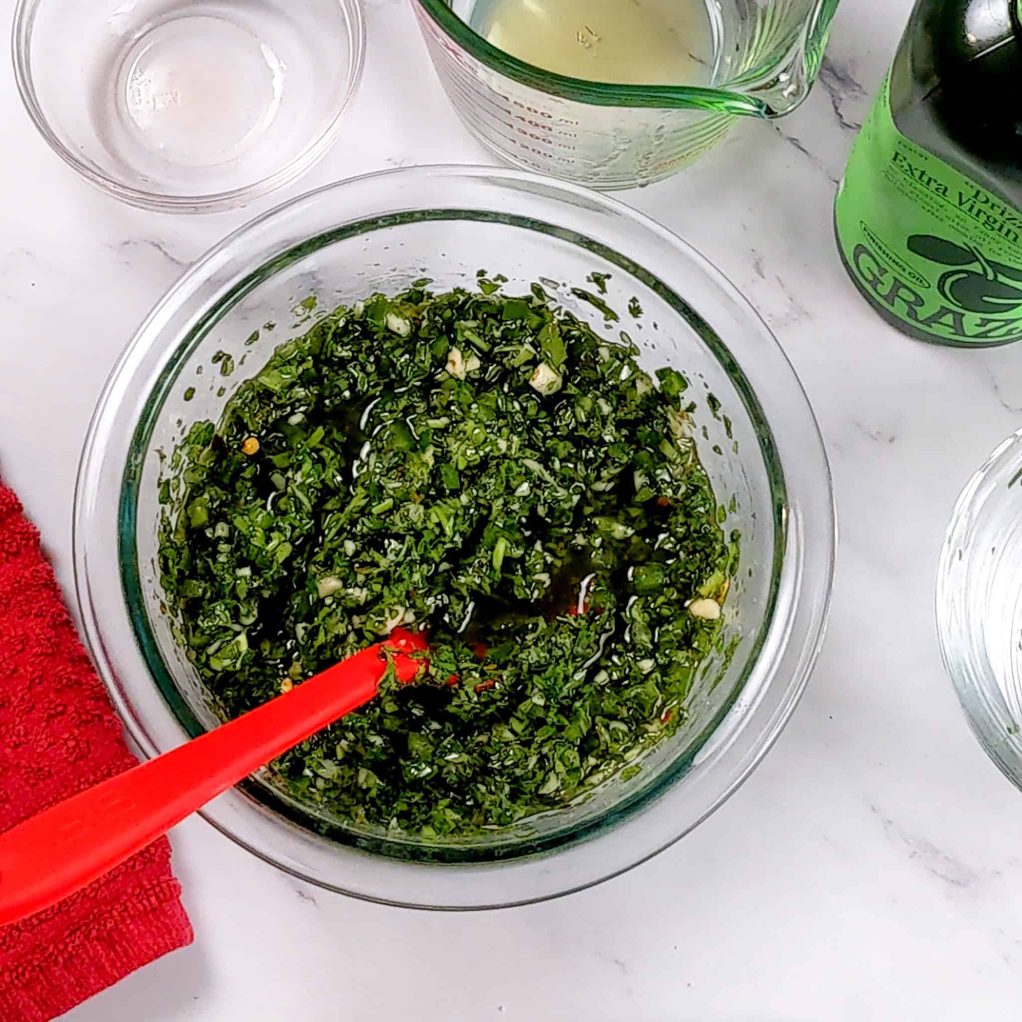 jalapeno chimichurri sauce in a glass mixing bowl with a silicone spoon.